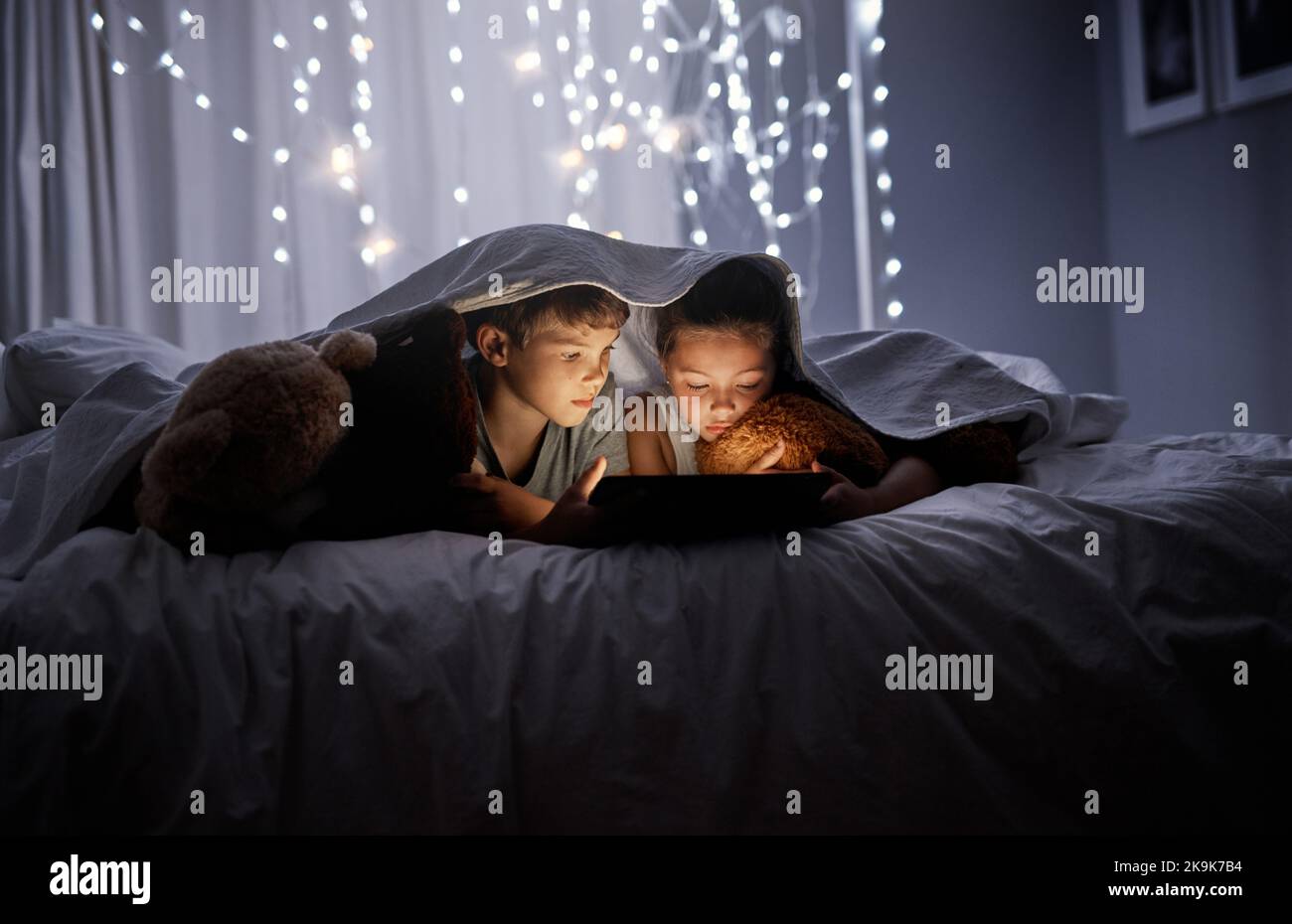 Questi fratelli amano i loro cartoni animati, due adorabili fratelli che usano un tablet digitale insieme a letto di notte. Foto Stock