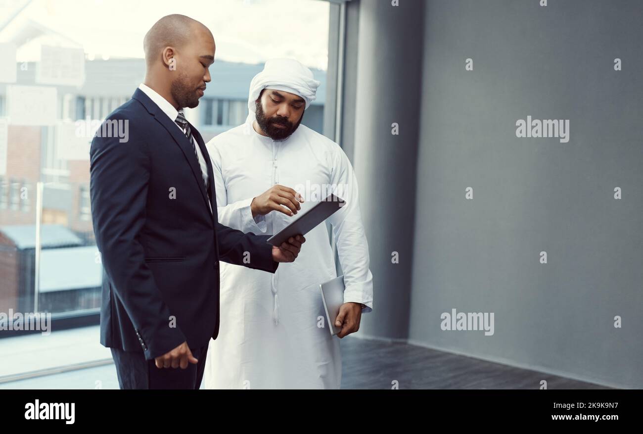 Il successo della loro azienda dipende dalla sua cultura collaborativa. Due uomini d'affari che utilizzano un tablet digitale mentre discutono in un ufficio moderno. Foto Stock