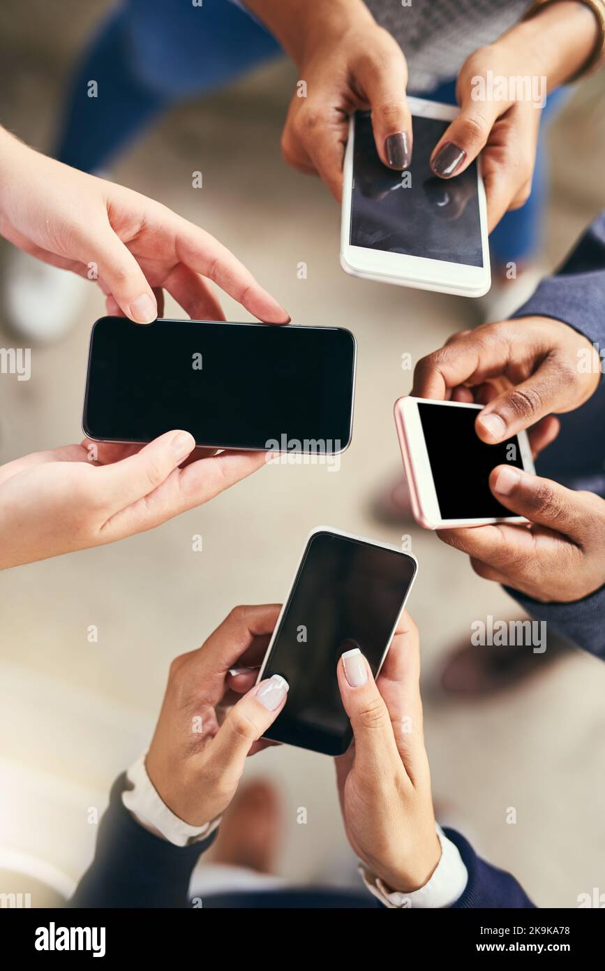 Questo è il modo in cui parliamo tra di noi in questi giorni. Inquadratura ad angolo alto di un gruppo di persone irriconoscibili che sfogliano e testano i loro cellulari Foto Stock