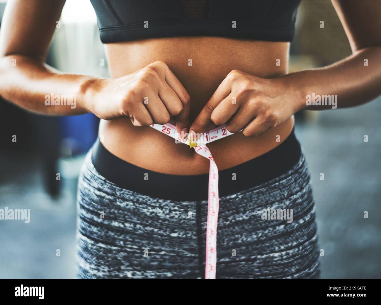 Quando la vostra routine di allenamento inizia a mostrare i risultati. Una giovane donna in forma che misura la vita in palestra. Foto Stock