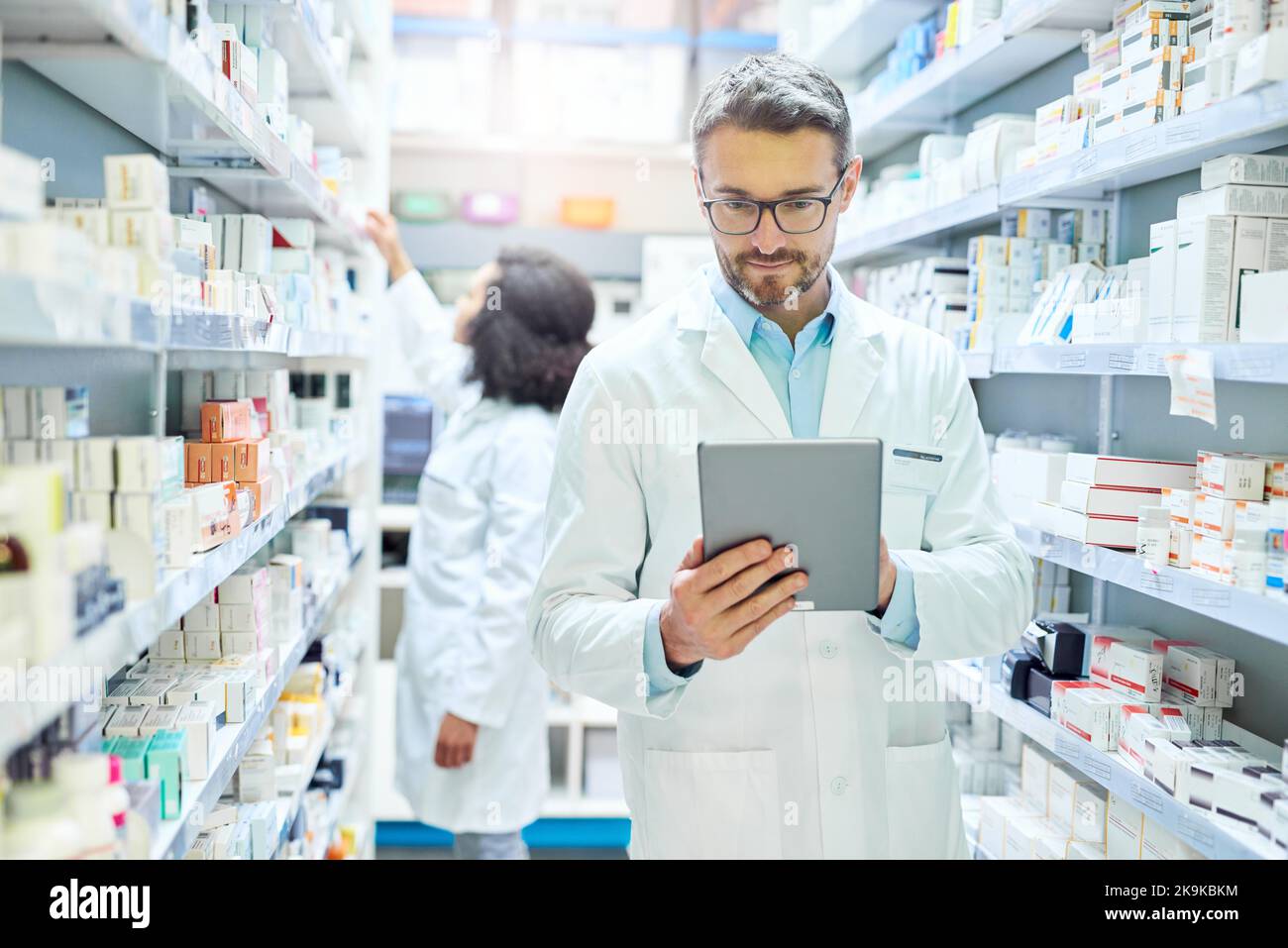 Un uomo maturo che usa un tablet digitale per fare inventario in farmacia. Foto Stock