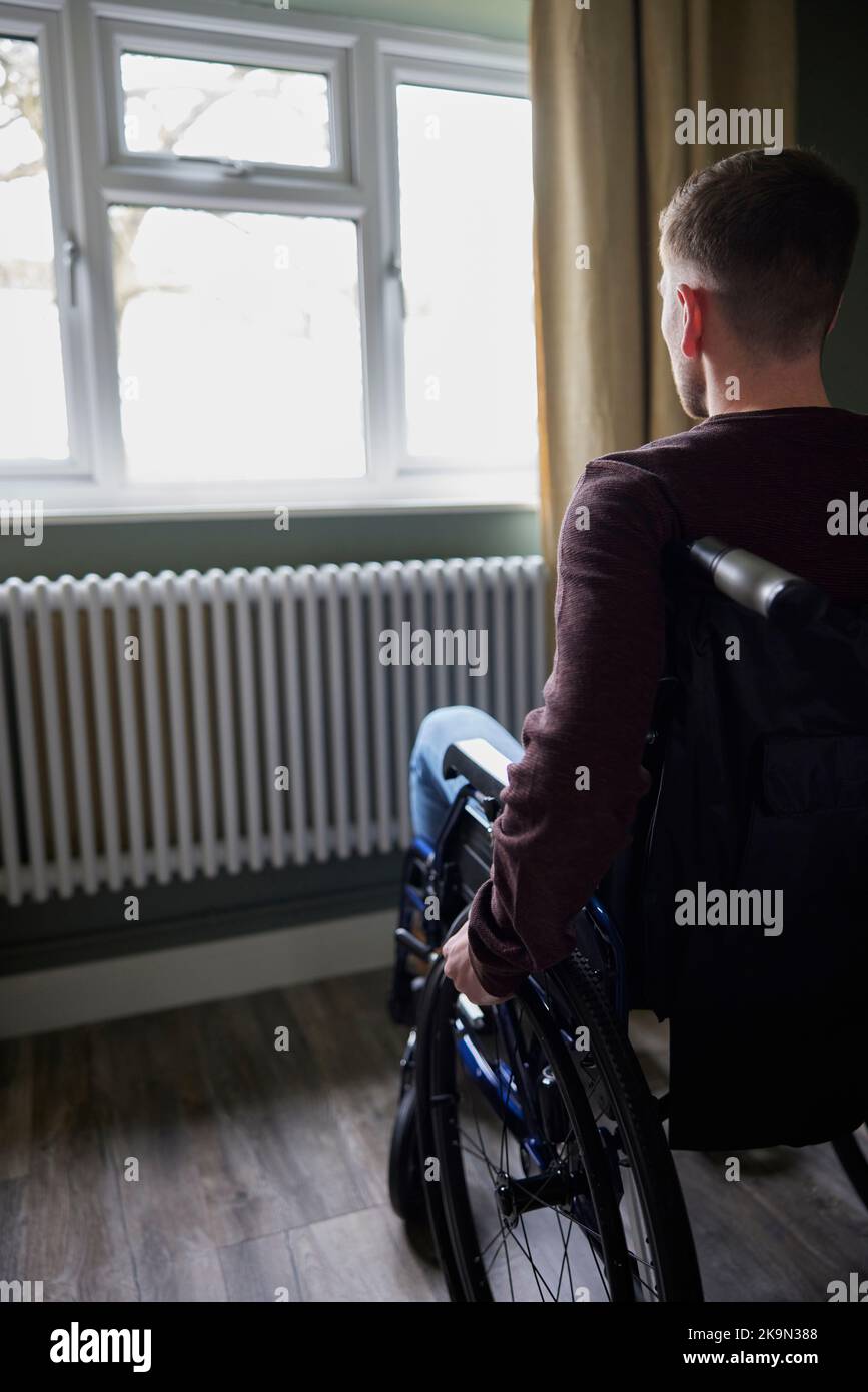 Vista posteriore dell'uomo depresso con la salute mentale povera in sedia a rotelle dalla finestra a casa Foto Stock