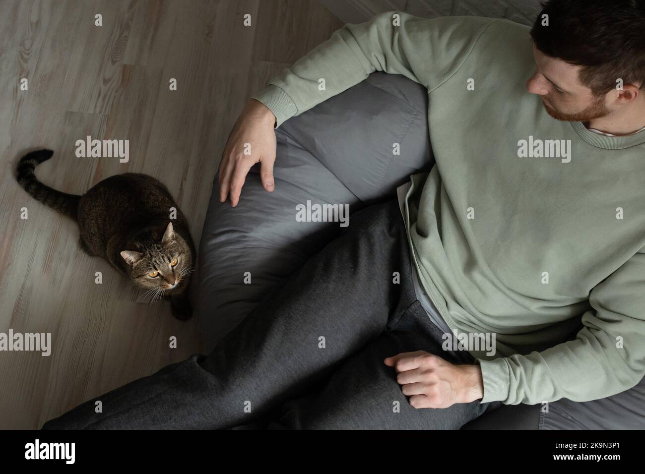 il proprietario è seduto su una sedia per borse e il suo gatto è seduto accanto a lui. Foto Stock