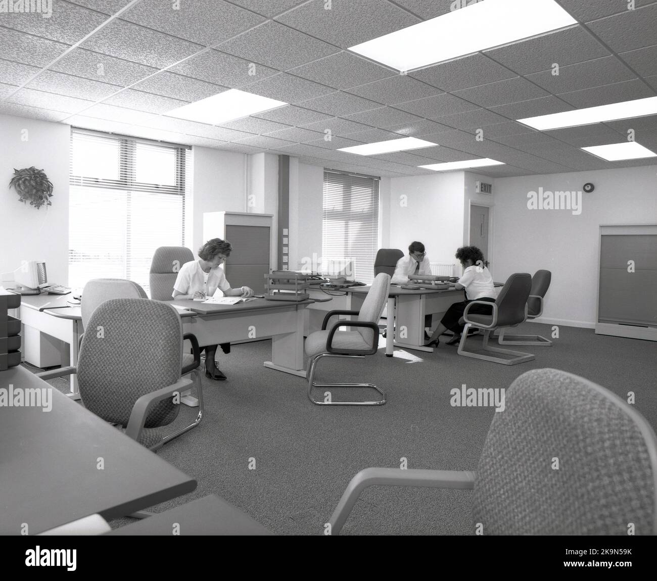 1989, storico, un maschio e una femmina che lavorano alle loro scrivanie in uno spazioso ufficio a pianta aperta, Inghilterra, Regno Unito. Grandi scrivanie semicircolari con sedie circostanti per riunioni informali - una che si svolge - e personal computer dell'epoca in mostra. Foto Stock