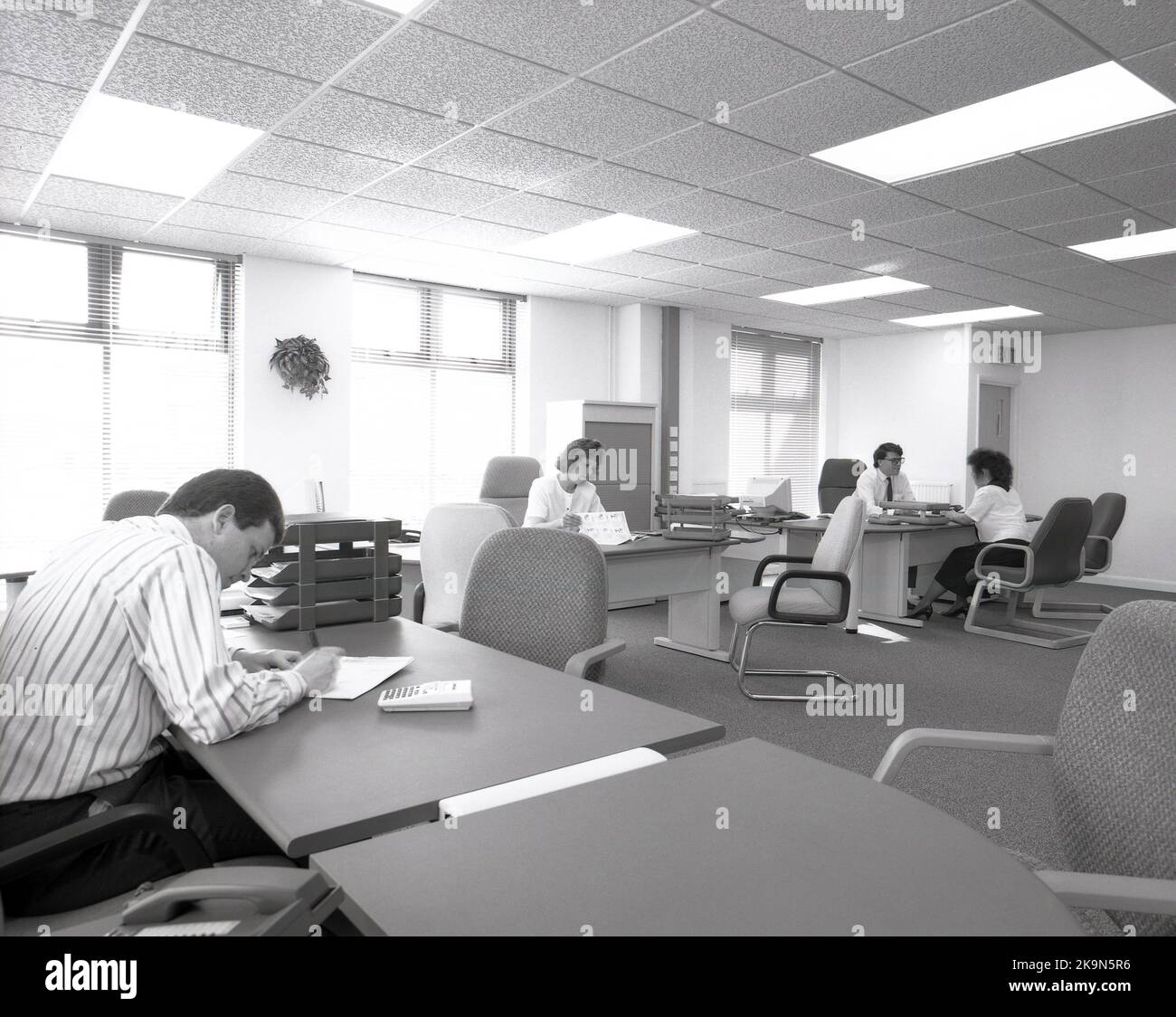 1989, dipendenti storici, di sesso maschile e femminile che lavorano alle loro scrivanie in uno spazioso ufficio a pianta aperta, Inghilterra, Regno Unito. Si possono vedere grandi scrivanie semicircolari con sedie circostanti per riunioni informali e personal computer dell'epoca. Foto Stock