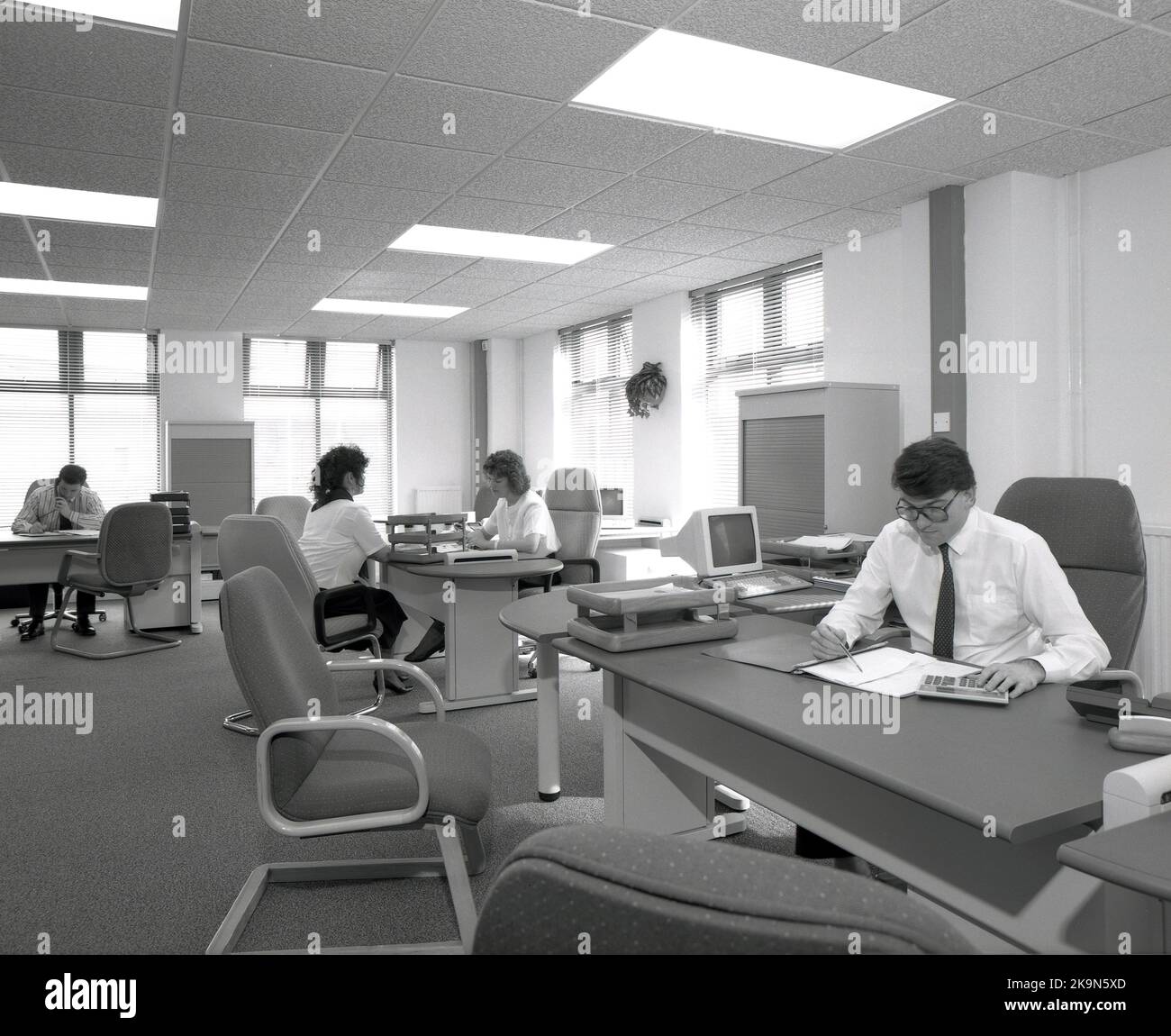 1989, dipendenti storici, di sesso maschile e femminile che lavorano alle loro scrivanie in un ufficio a pianta aperta, Inghilterra, Regno Unito. Nella foto si possono vedere i personal computer dell'epoca Foto Stock