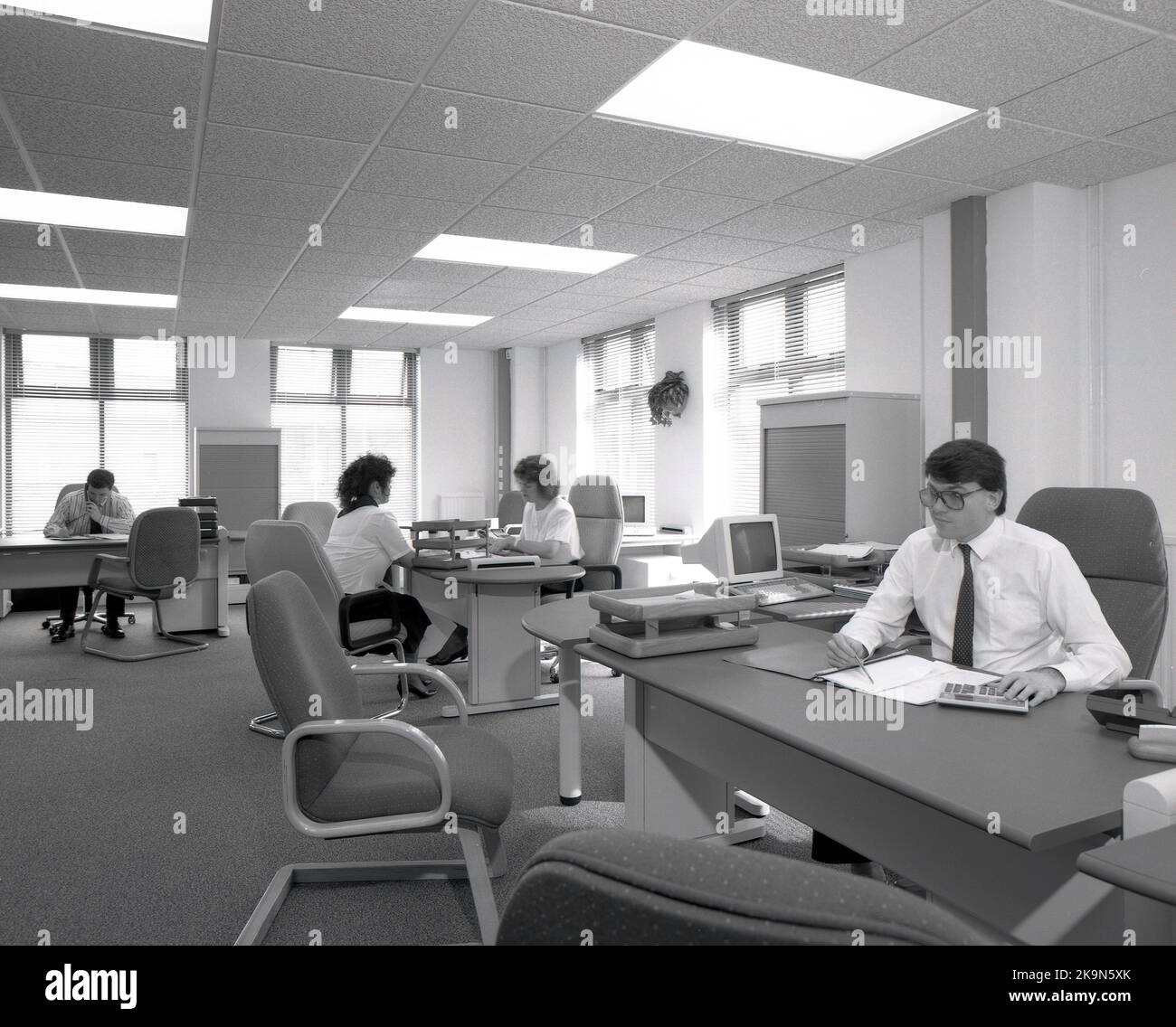 1989, dipendenti storici, di sesso maschile e femminile che lavorano alle loro scrivanie in un ufficio a pianta aperta, Inghilterra, Regno Unito. Nella foto si possono vedere i personal computer dell'epoca Foto Stock