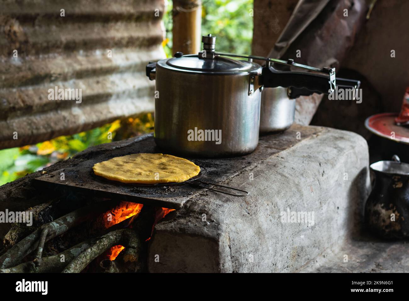 Cucina tradizionale in una fattoria colombiana, con una tostatura arepa accanto a un fornello a pressione su una stufa di mattoni fatti a mano ricoperta di cenere grigia. Foto Stock
