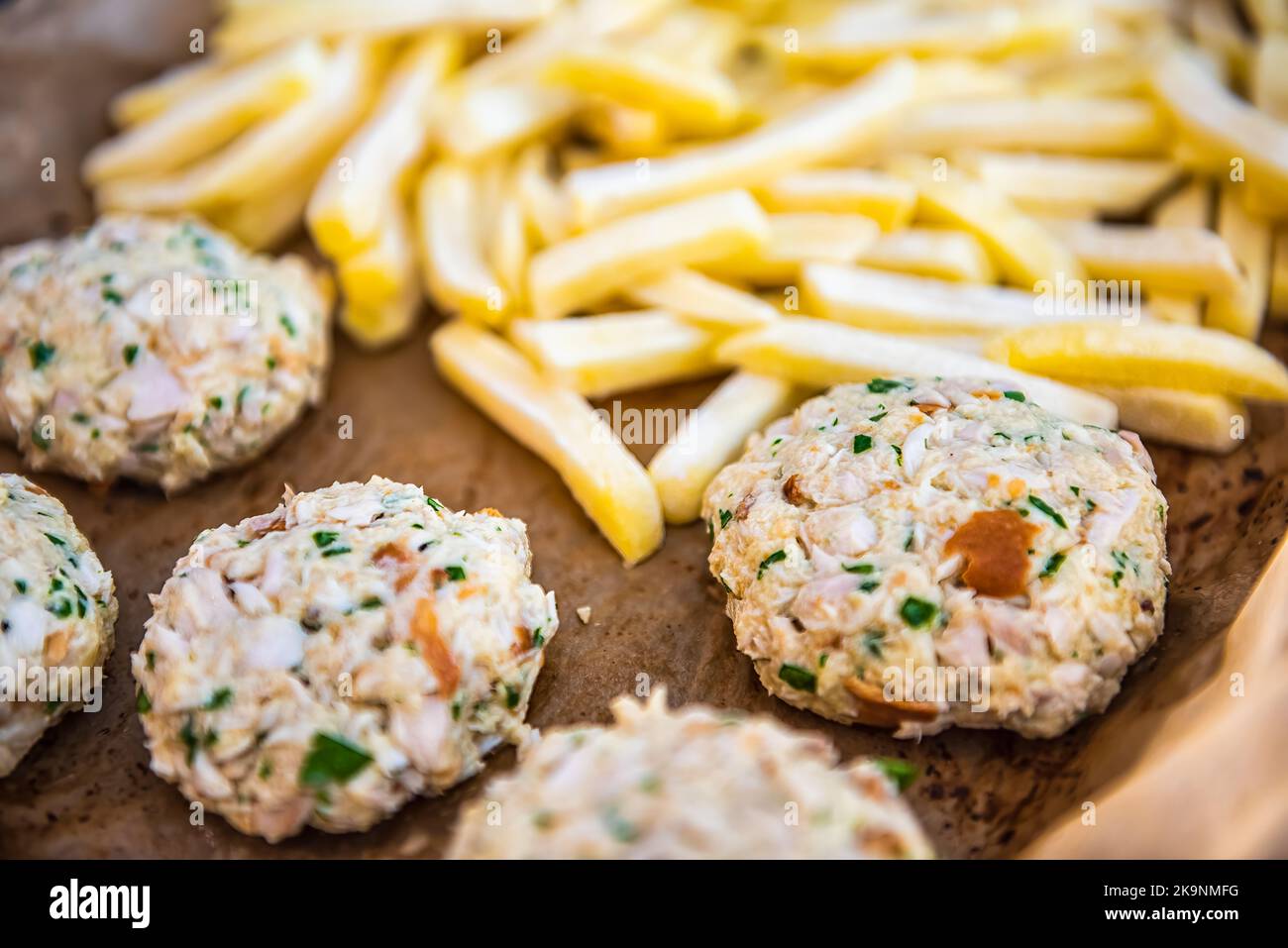 Macro closeup di patatine fritte surgelate, torte di granchio di pesce crudo su vassoio da forno carta pergamena per forno prima di cucinare come pasto di pesce tradizionale Foto Stock