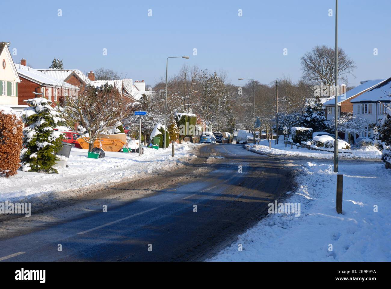 Una strada suburbana ricurva e residenziale dopo la nevicata, con la neve sul fondo della strada che si trasforma in fanghiglia e spazzatura fuori per la raccolta Foto Stock