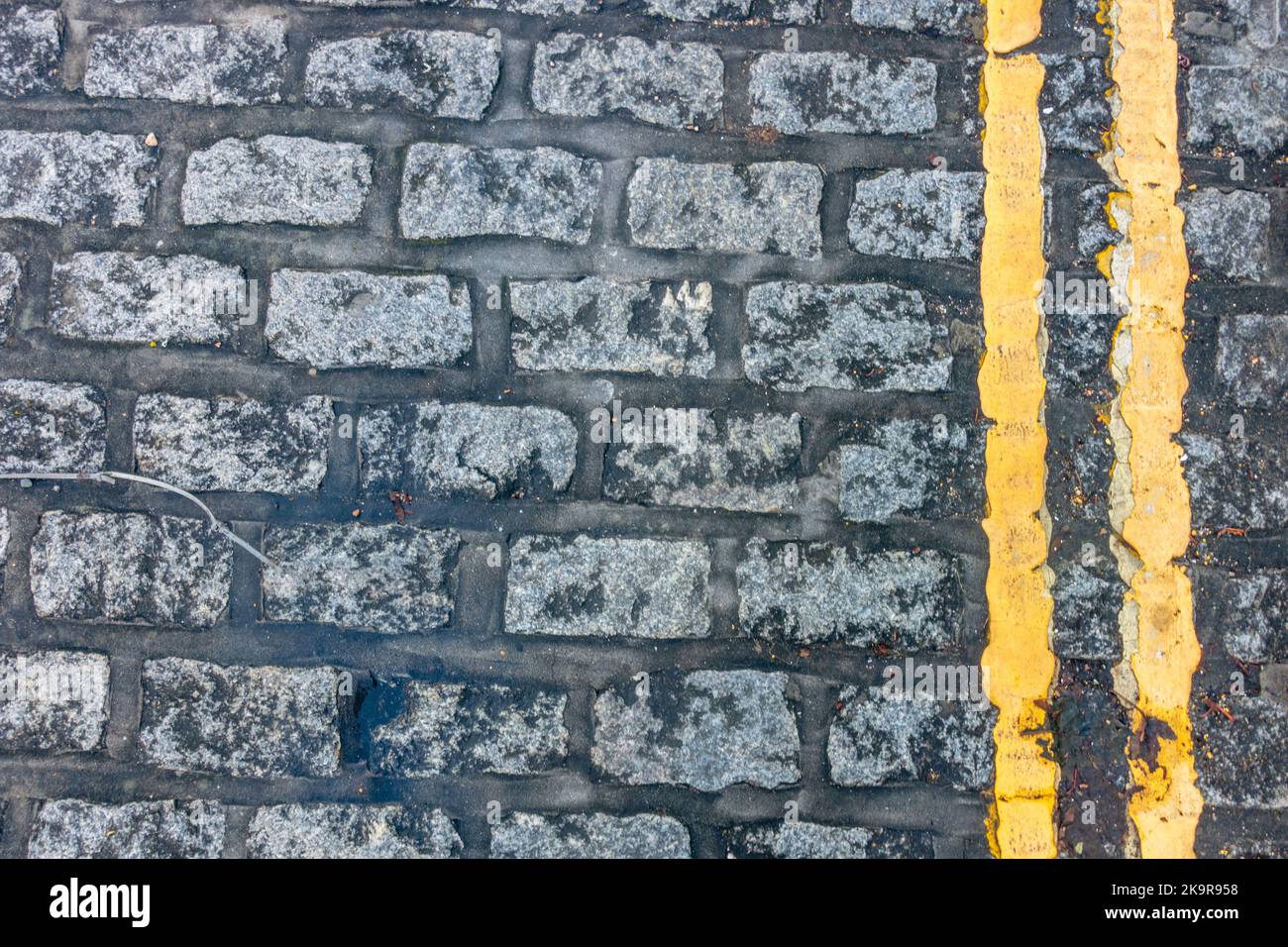 Guardando verso il basso le doppie linee gialle dipinte lungo il bordo di una strada acciottolata. Foto Stock