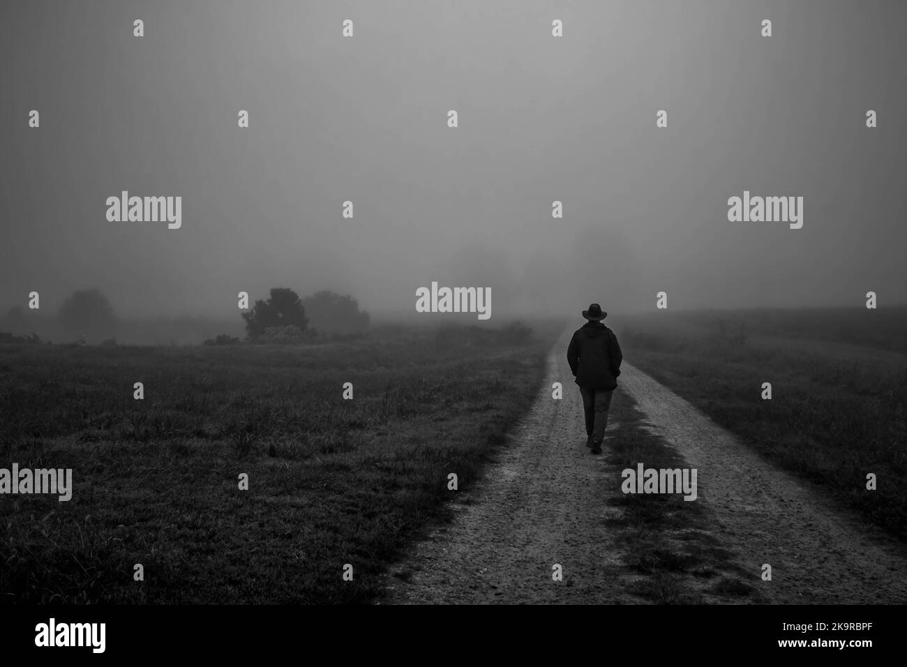 Un'atmosfera da moody mentre un uomo sfreccia lungo una strada sterrata su una mattina di nebbia calma. Uomo che cammina via. Foto Stock