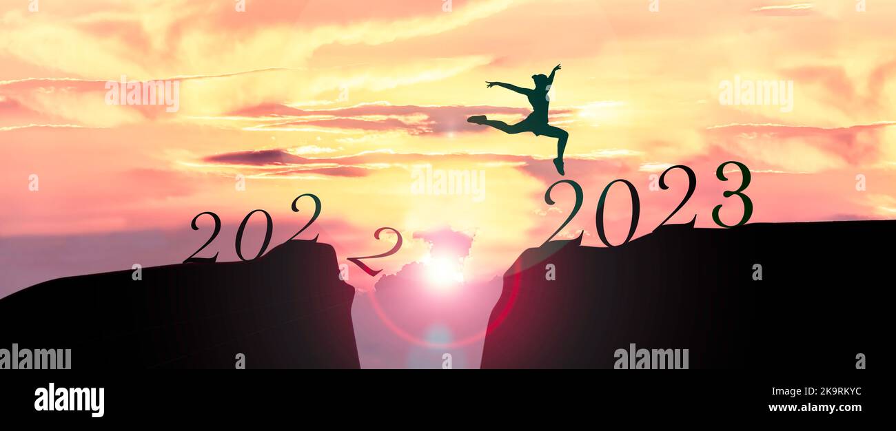 2023 concetto felice di nuovo anno, giovane donna che saltano attraverso il divario della montagna dal vecchio anno 2022 al nuovo anno 2023. Foto Stock