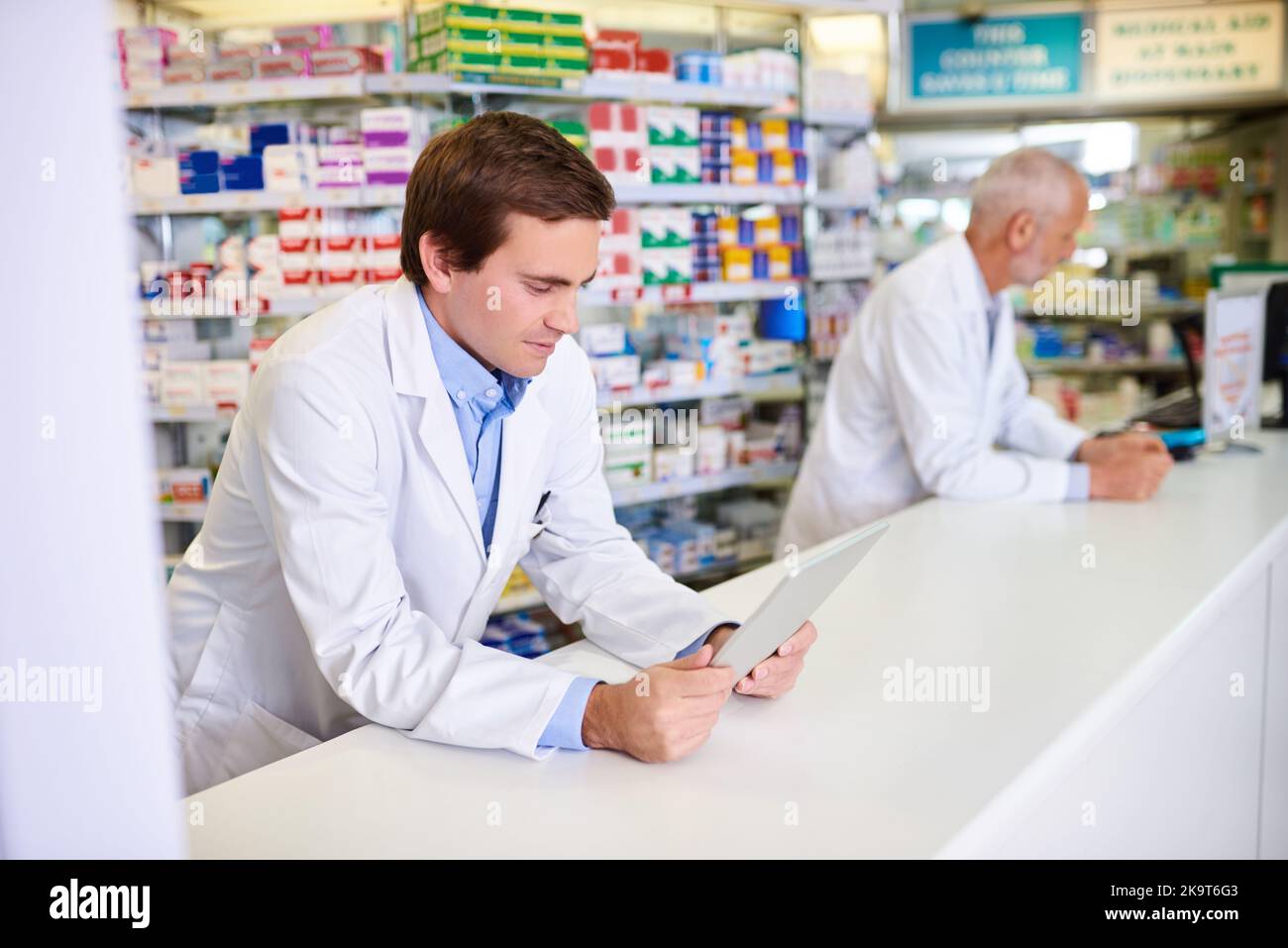 Introduzione della tecnologia wireless nel mondo farmaceutico: Un giovane farmacista che utilizza un tablet digitale mentre si trova in farmacia. Foto Stock