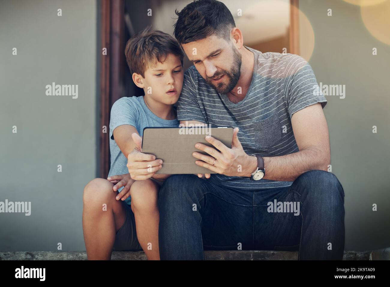 Unire il tempo nell'era digitale: Un padre e un figlio che usano un tablet digitale insieme sui gradini più frontali della loro casa. Foto Stock