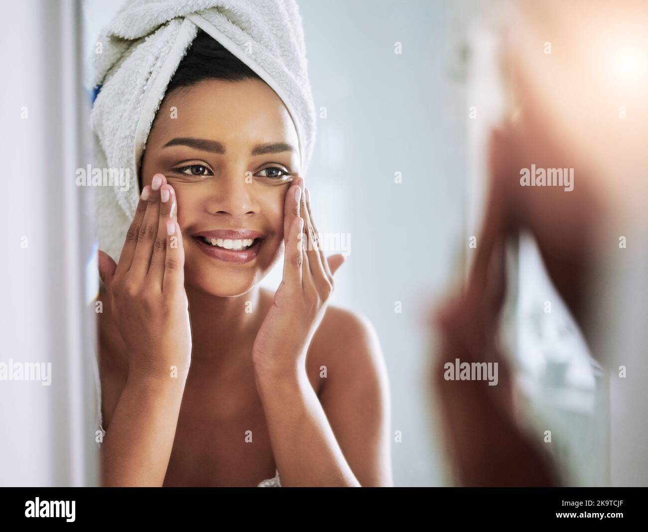 Il suo così liscio quando il relativo nutrito. Una giovane donna attraente che applica il moisturizer al suo viso nel bagno. Foto Stock