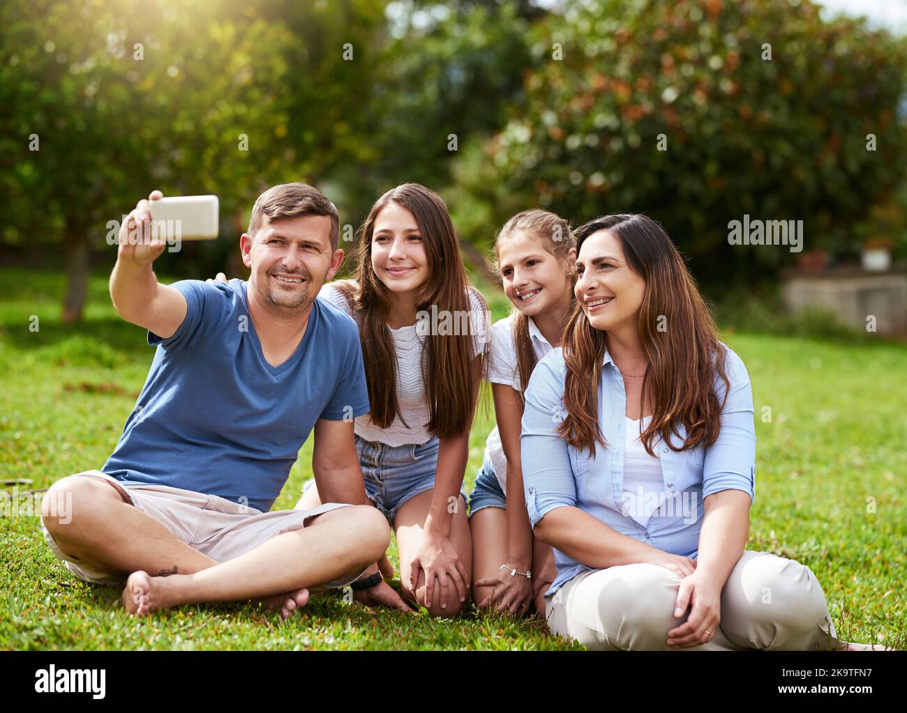 Tempo per una foto di famiglia. Una famiglia allegra seduto in un parco mentre si scatta un autoritratto insieme fuori durante il giorno. Foto Stock
