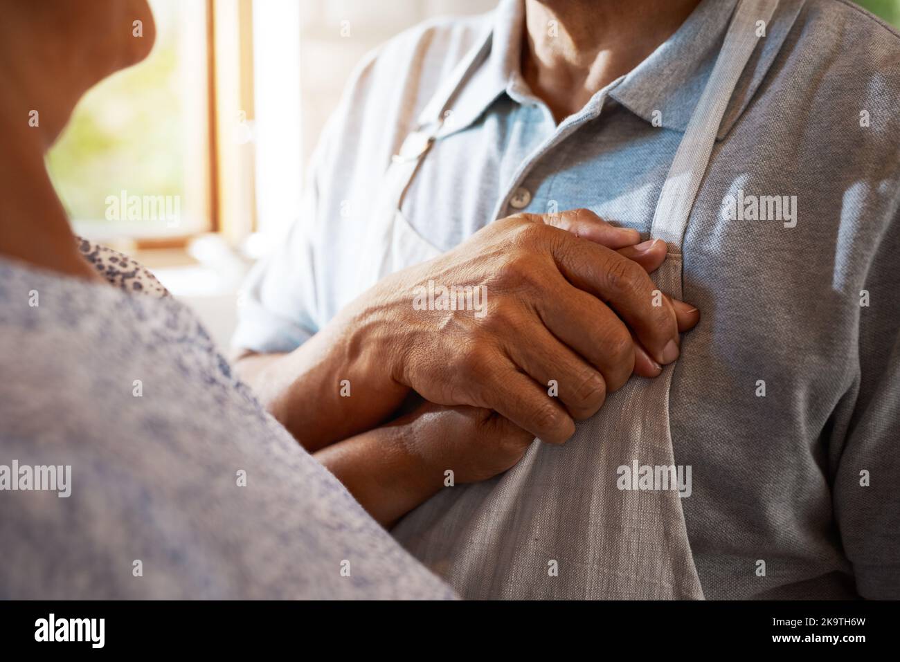 Non sei nel mio cuore, tu sei il mio cuore, un uomo maturo che tiene la mano delle sue mani vicino al suo cuore nella cucina di casa. Foto Stock
