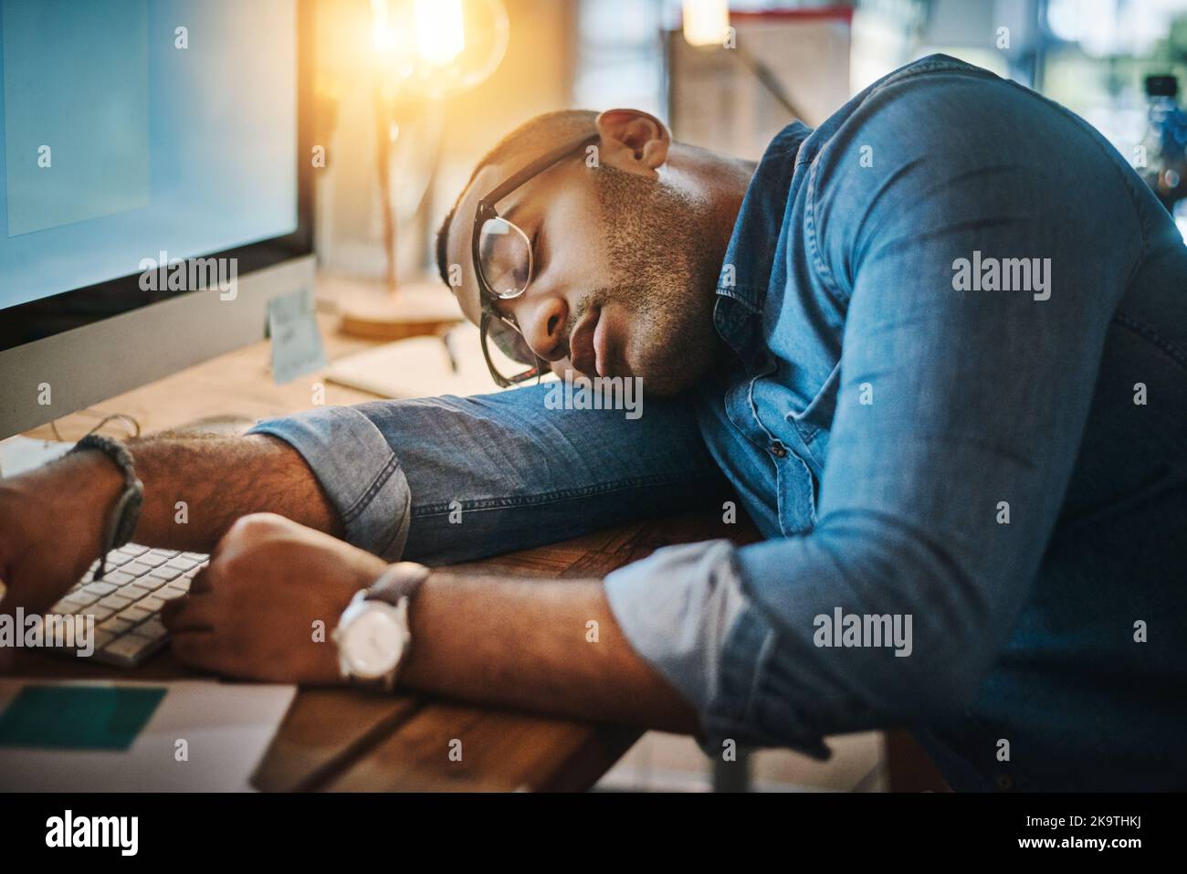 La sua scrivania sarà il suo cuscino per la notte, un giovane uomo d'affari esausto che dorme alla sua scrivania in un ufficio moderno. Foto Stock