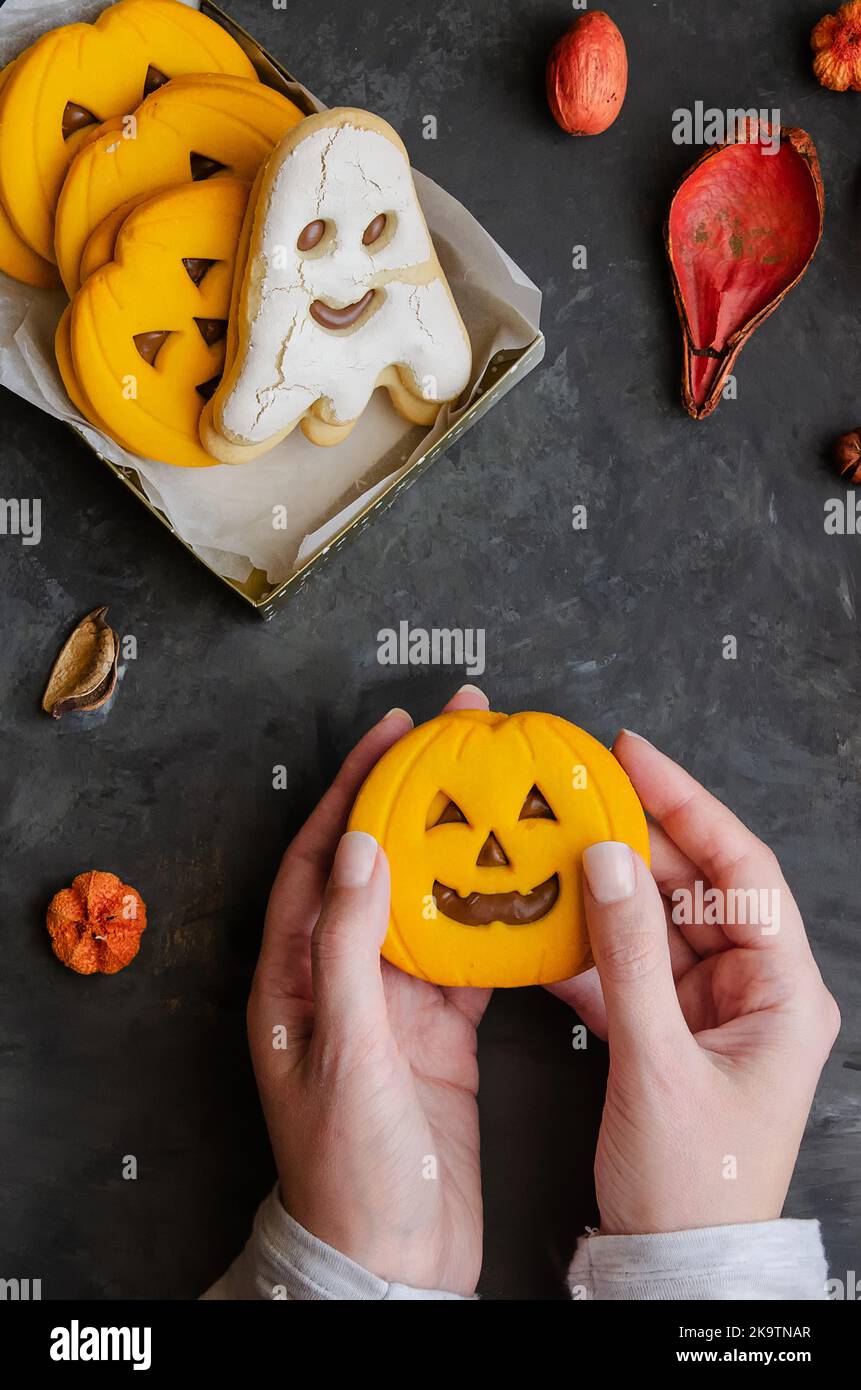 Mani femminili che tengono il biscotto spaventoso della zucca sul fondo scuro con la decorazione della sabbia del simbolo di Halloween. Happy Halloween concetto. Foto Stock