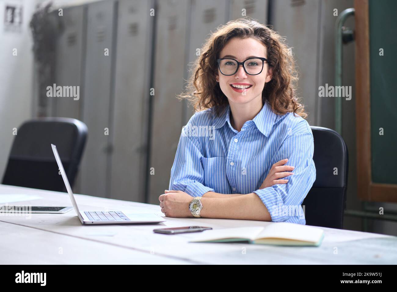 Giovane donna felice insegnante on-line seduto alla scrivania con un computer portatile. Verticale Foto Stock