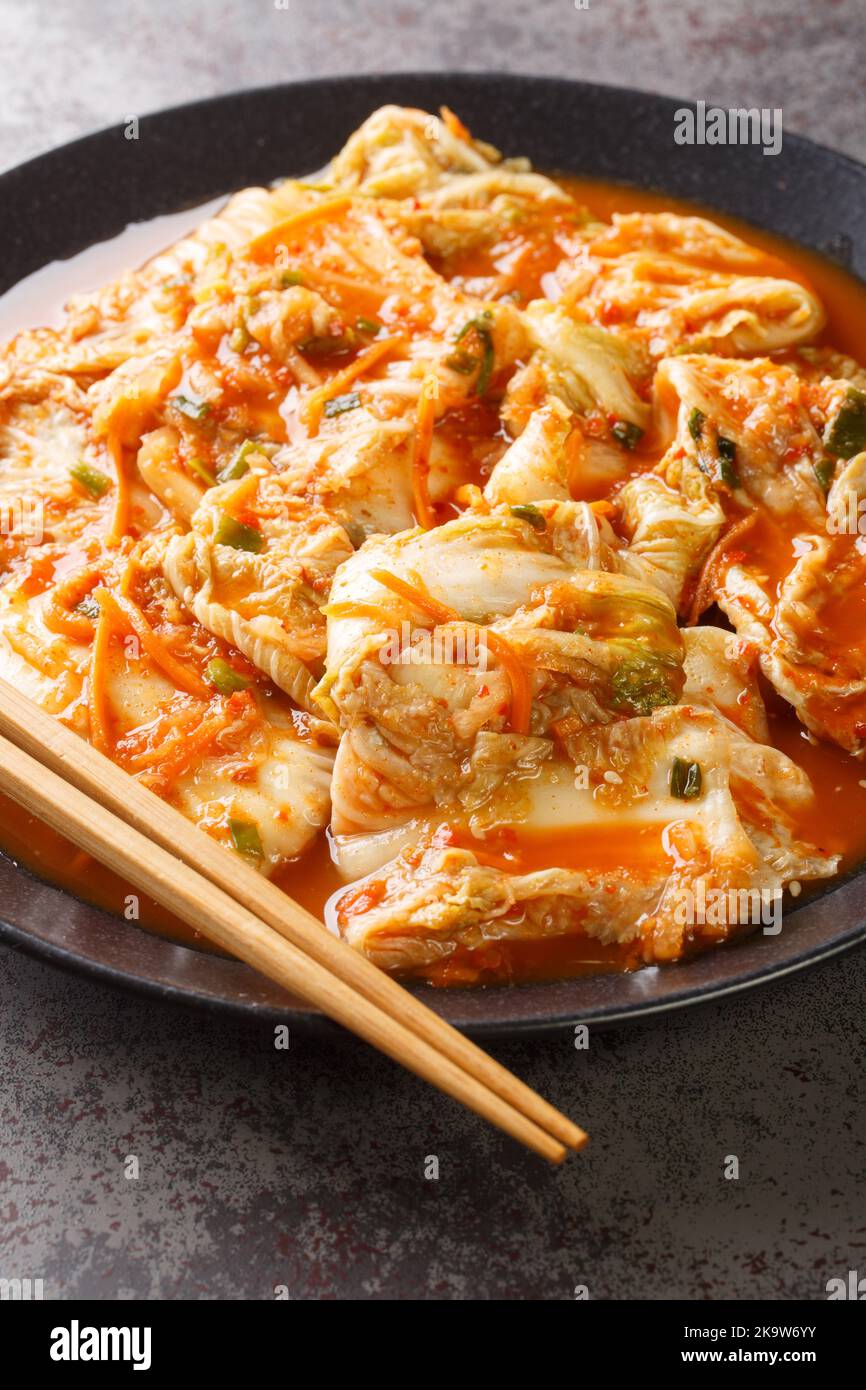 Mangiare cavolo kimchi in una ciotola con bacchette, primi piatti coreani in un piatto nero su un tavolo. Verticale Foto Stock
