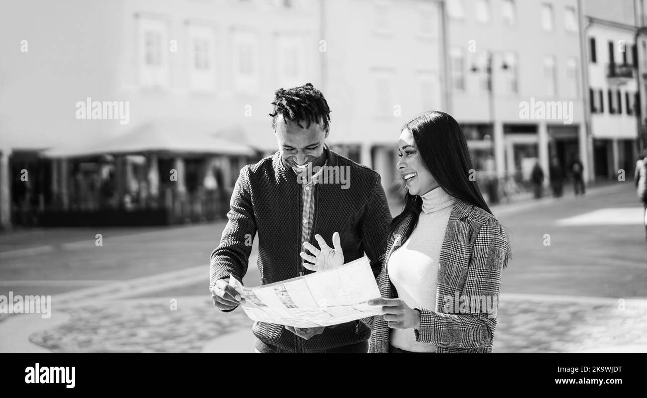 Felice coppia africana che ha divertimento guardando la mappa della città durante le vacanze di viaggio - fuoco sul volto della donna - montaggio in bianco e nero Foto Stock
