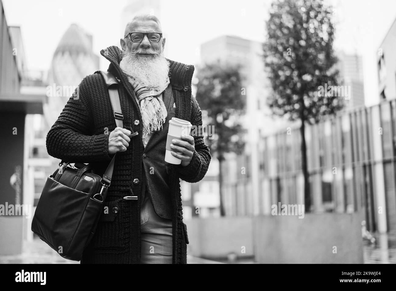 Buon uomo d'affari senior che cammina per lavorare nel giorno delle piogge autunnali - Soft focus sulla barba - montaggio in bianco e nero Foto Stock