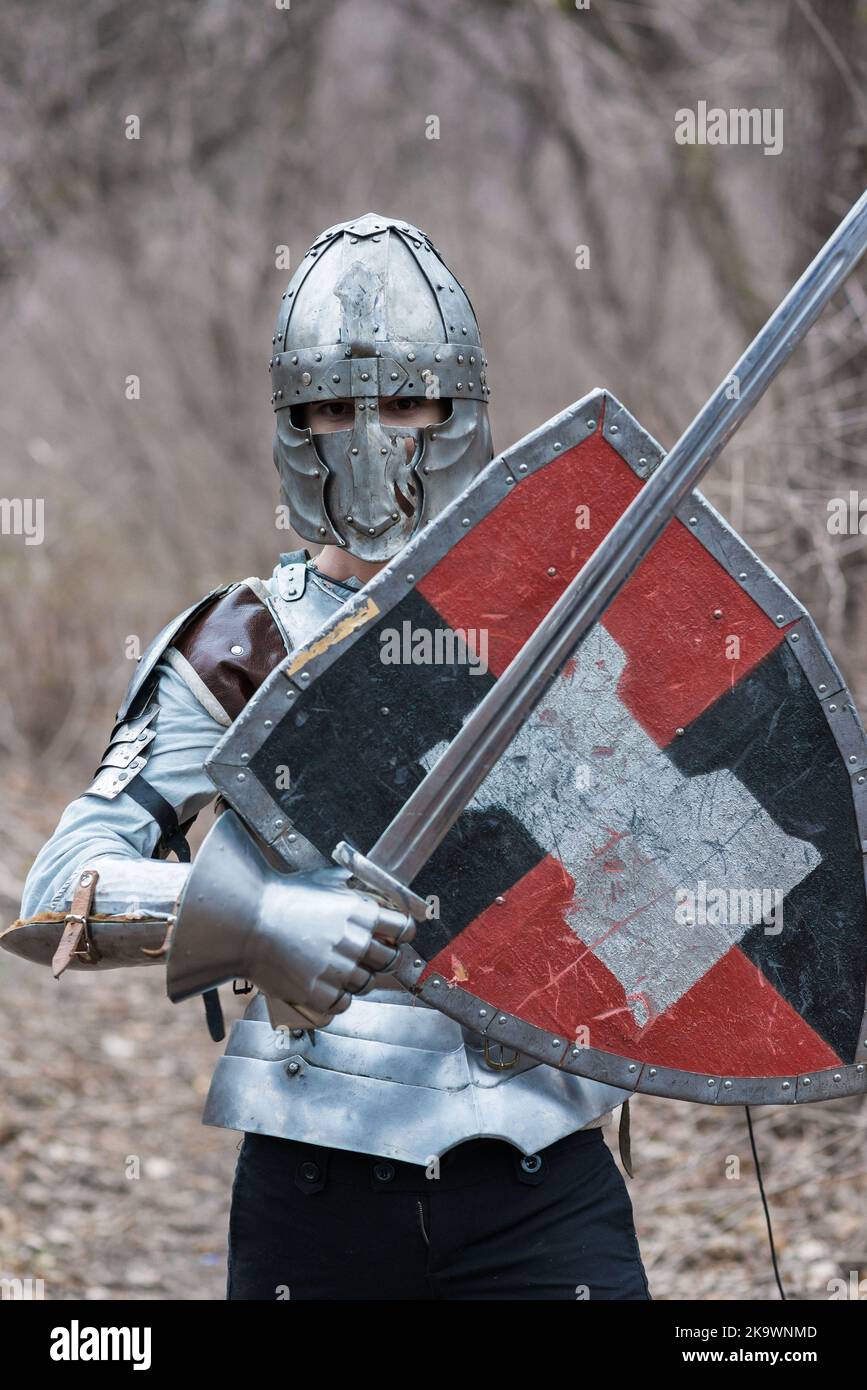 Nobile guerriero. Ritratto di un guerriero o cavaliere medeivale in armatura e casco con scudo e spada in posa isolata su sfondo scuro. Foto Stock