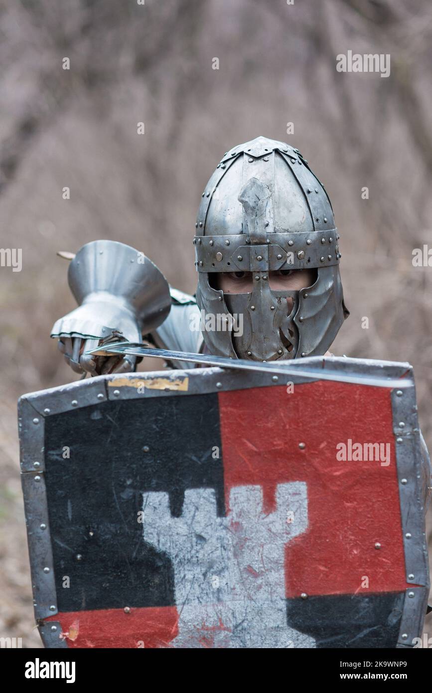 Nobile guerriero. Ritratto di un guerriero o cavaliere medeivale in armatura e casco con scudo e spada in posa isolata su sfondo scuro. Foto Stock