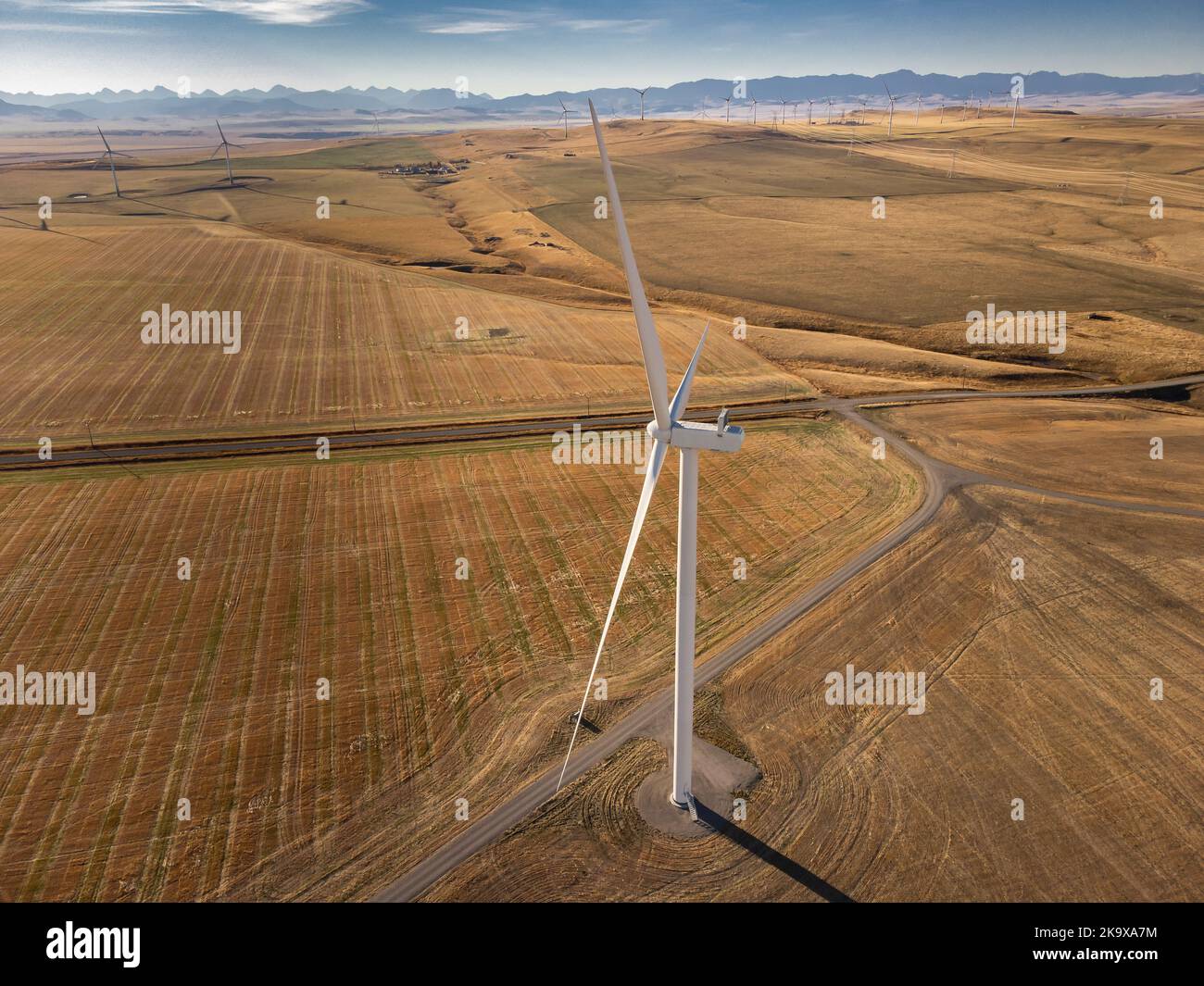 Vista dall'alto sopra una turbina eolica che si erge in alto sulle fattorie canadesi con le lontane Montagne Rocciose vicino a Pincher Creek Alberta Canada. Foto Stock