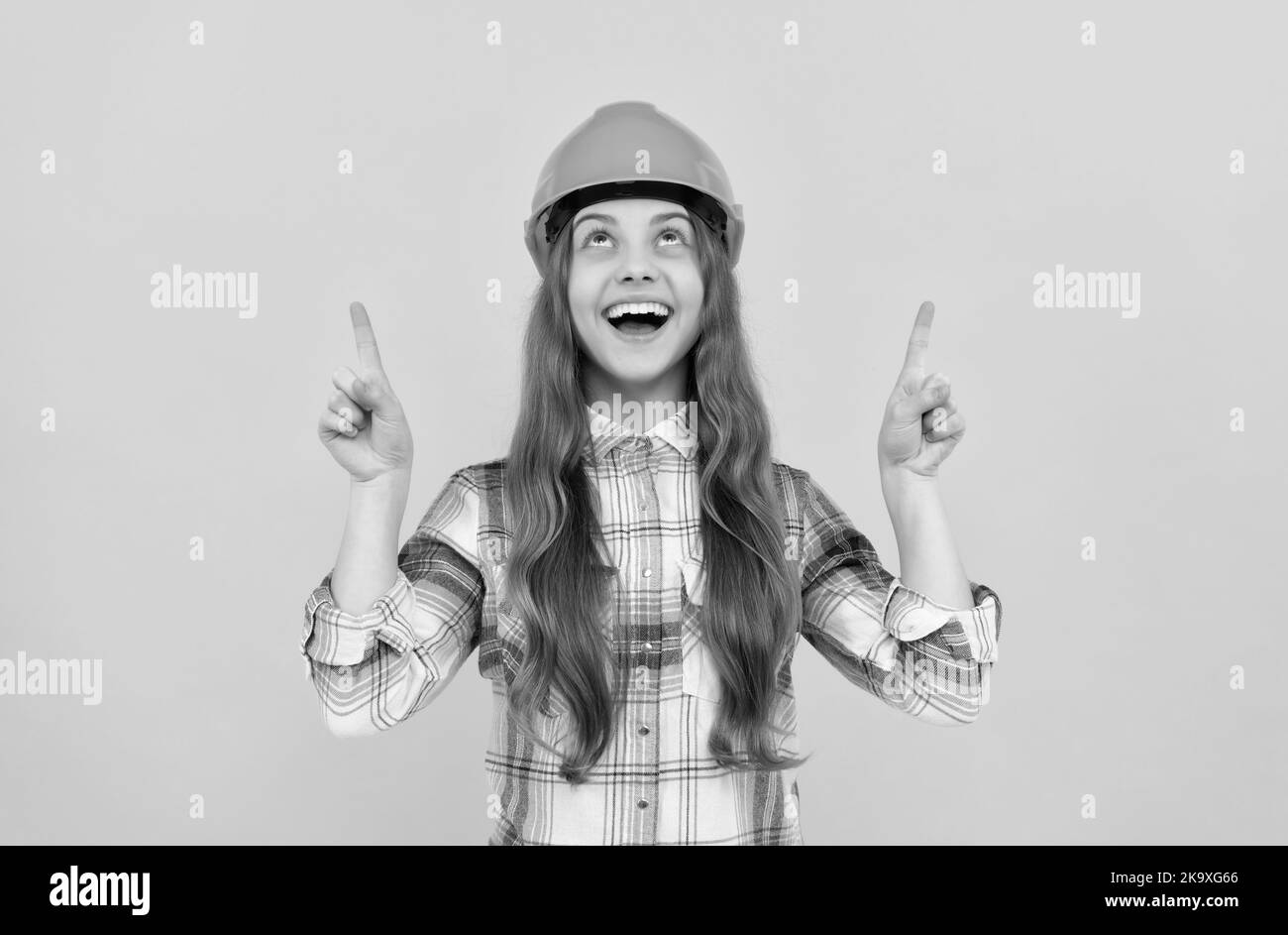 ragazza teen felice in casco e camicia a scacchi puntando il dito verso l'alto, dimostrare Foto Stock