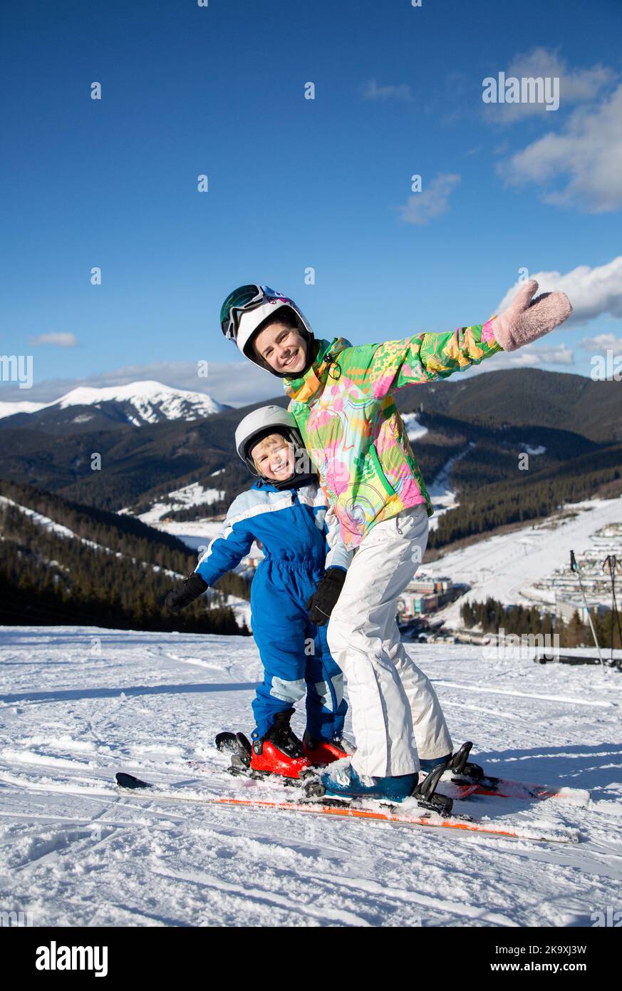 il bambino e la ragazza adolescente, fratello e sorella, si rilassano nella stazione sciistica, con gioia in piedi fianco a fianco sugli sci in cima alla pista di montagna. Inverno spa Foto Stock