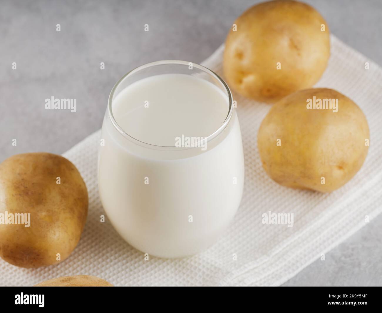 Latte di patate alternativa bevanda non lattiera. Latte senza lattosio e patate crude su sfondo grigio. Concetto di latte alternativo Foto Stock