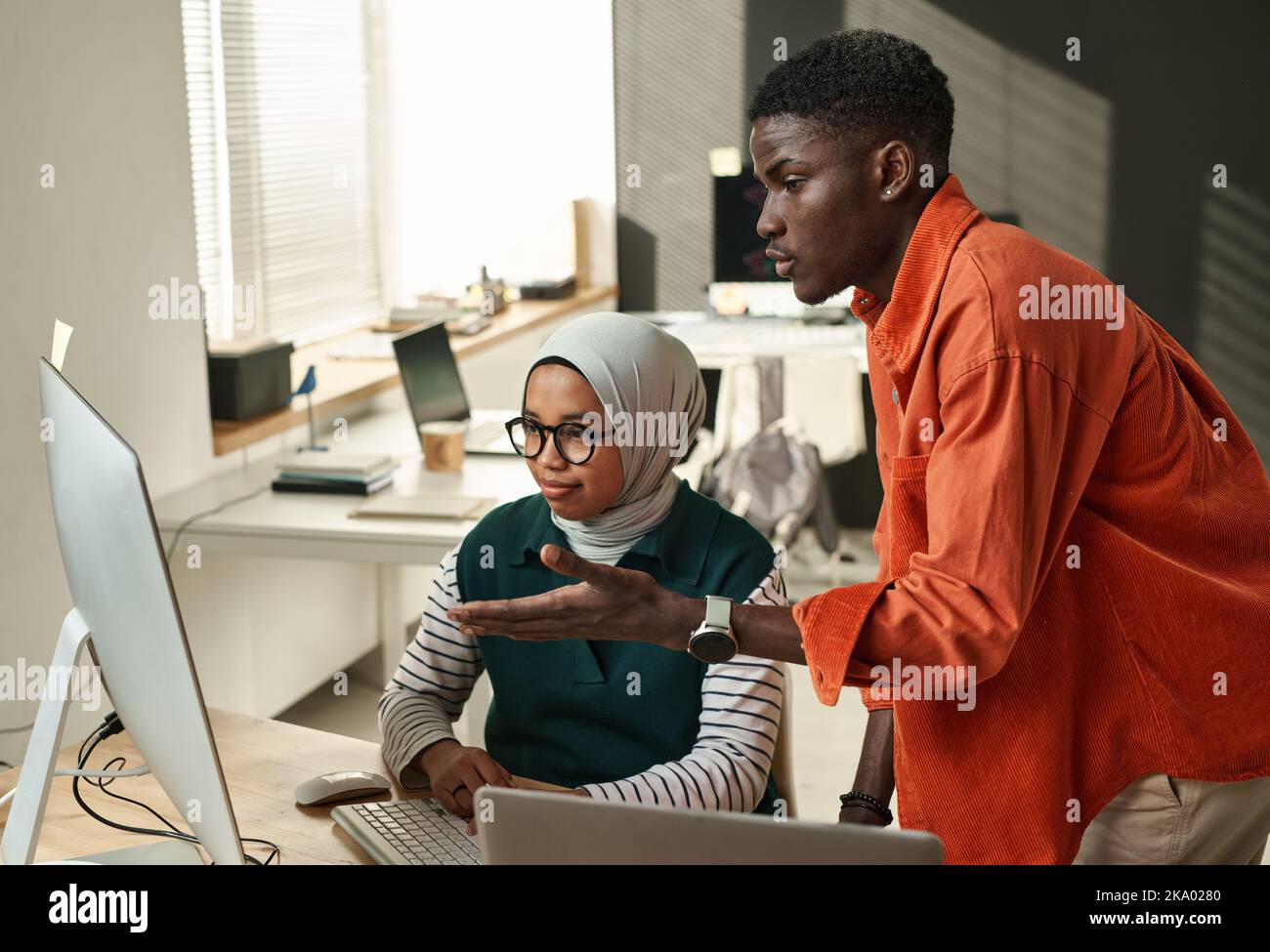 Giovane uomo d'affari fiducioso consulenza con una collega musulmana durante la presentazione di informazioni on-line o punti di progetto Foto Stock