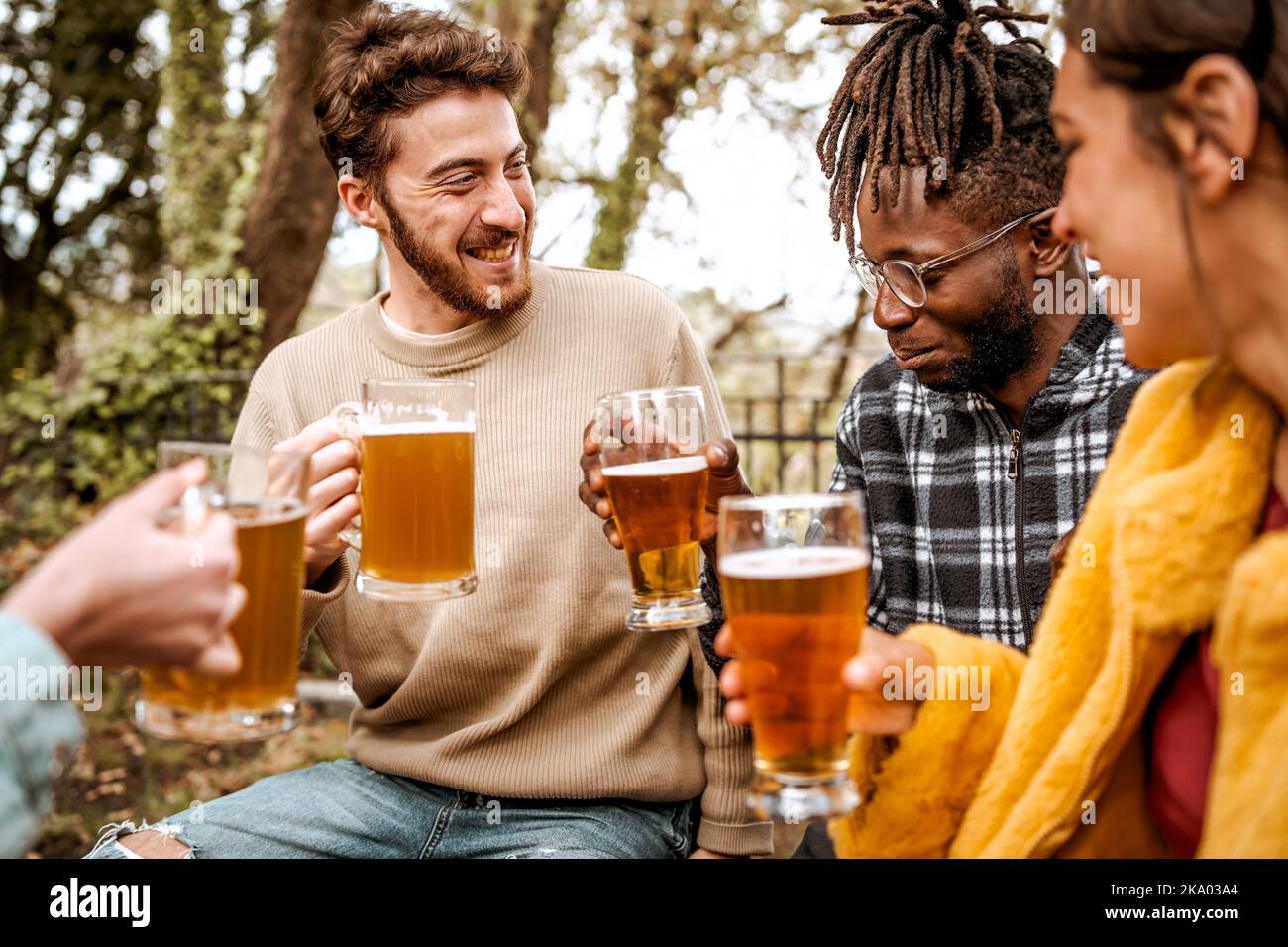 Gruppo multietnico di giovani amici che hanno una festa nella foresta pub divertirsi a parlare e bere birre - bevande alcoliche, diversità, benessere e pe Foto Stock