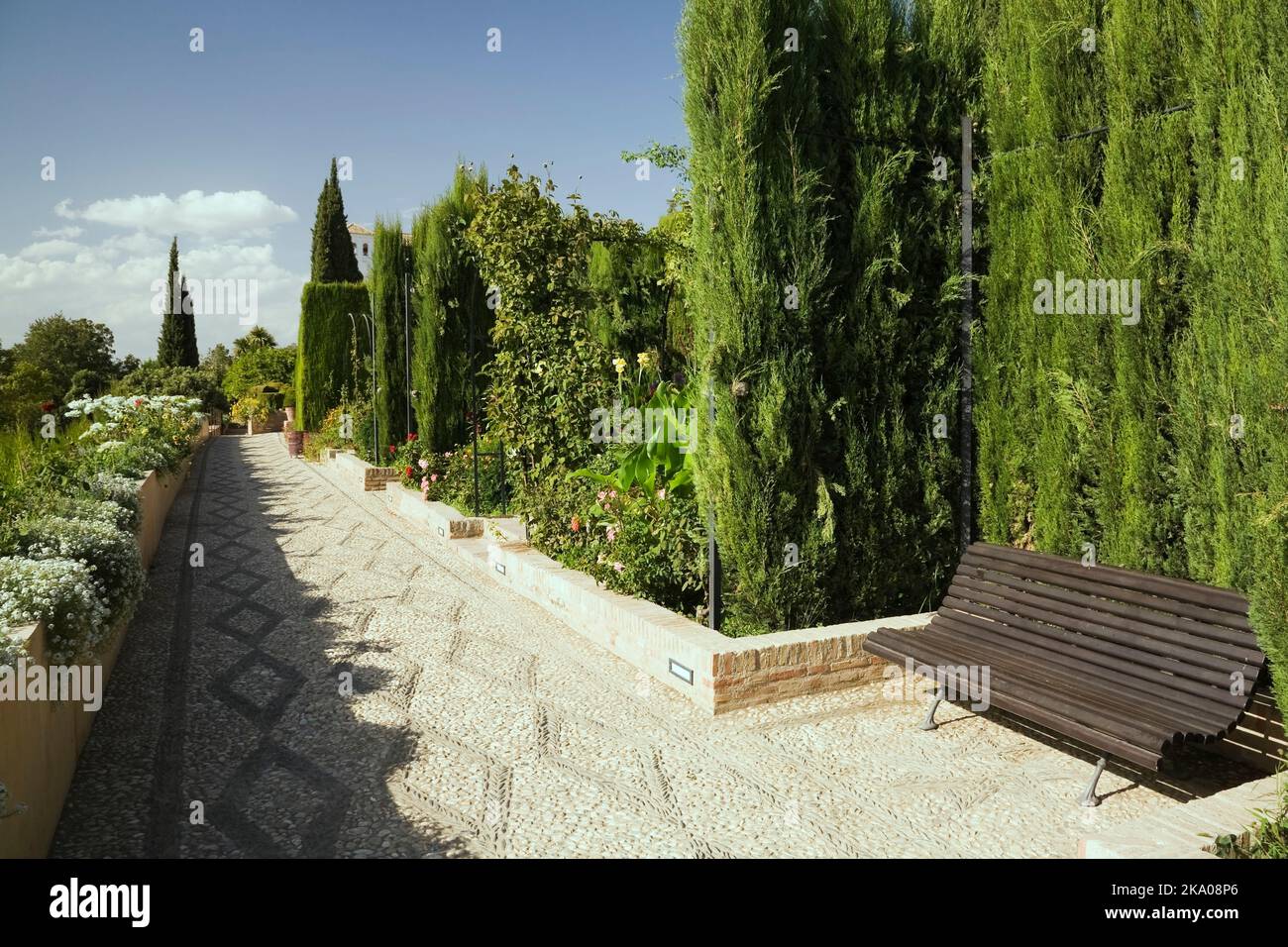 Panca in legno su una passeggiata lastricata di ciottoli in un giardino ornamentale sul palazzo Alhambra terreni, Granada, Spagna. Foto Stock