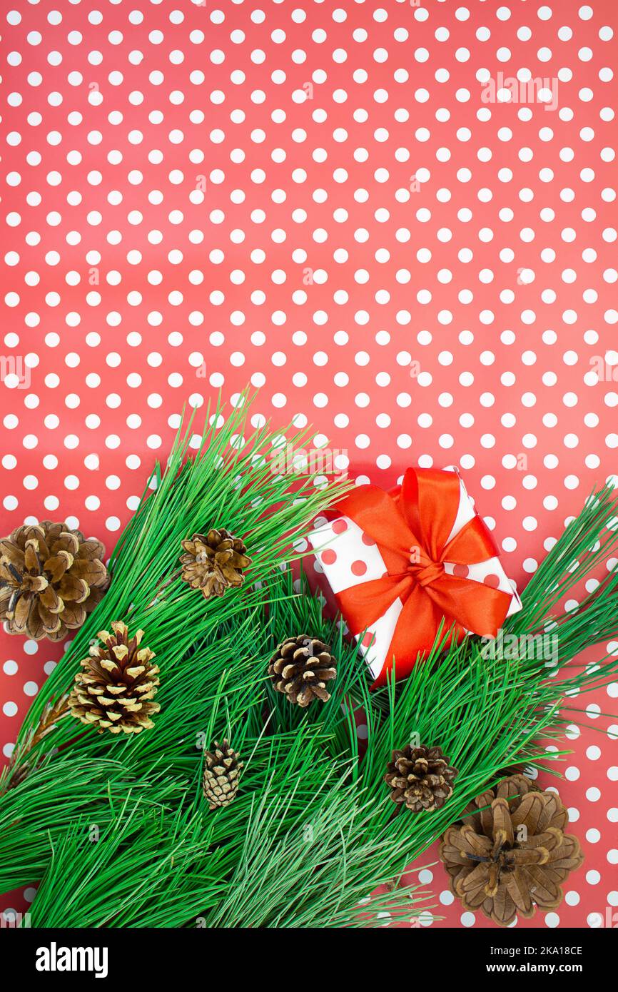 Rami di abete con coni, scatola regalo con arco su fondo rosso con puntini di polka. Natale, nuovo anno. Spazio di copia Foto Stock