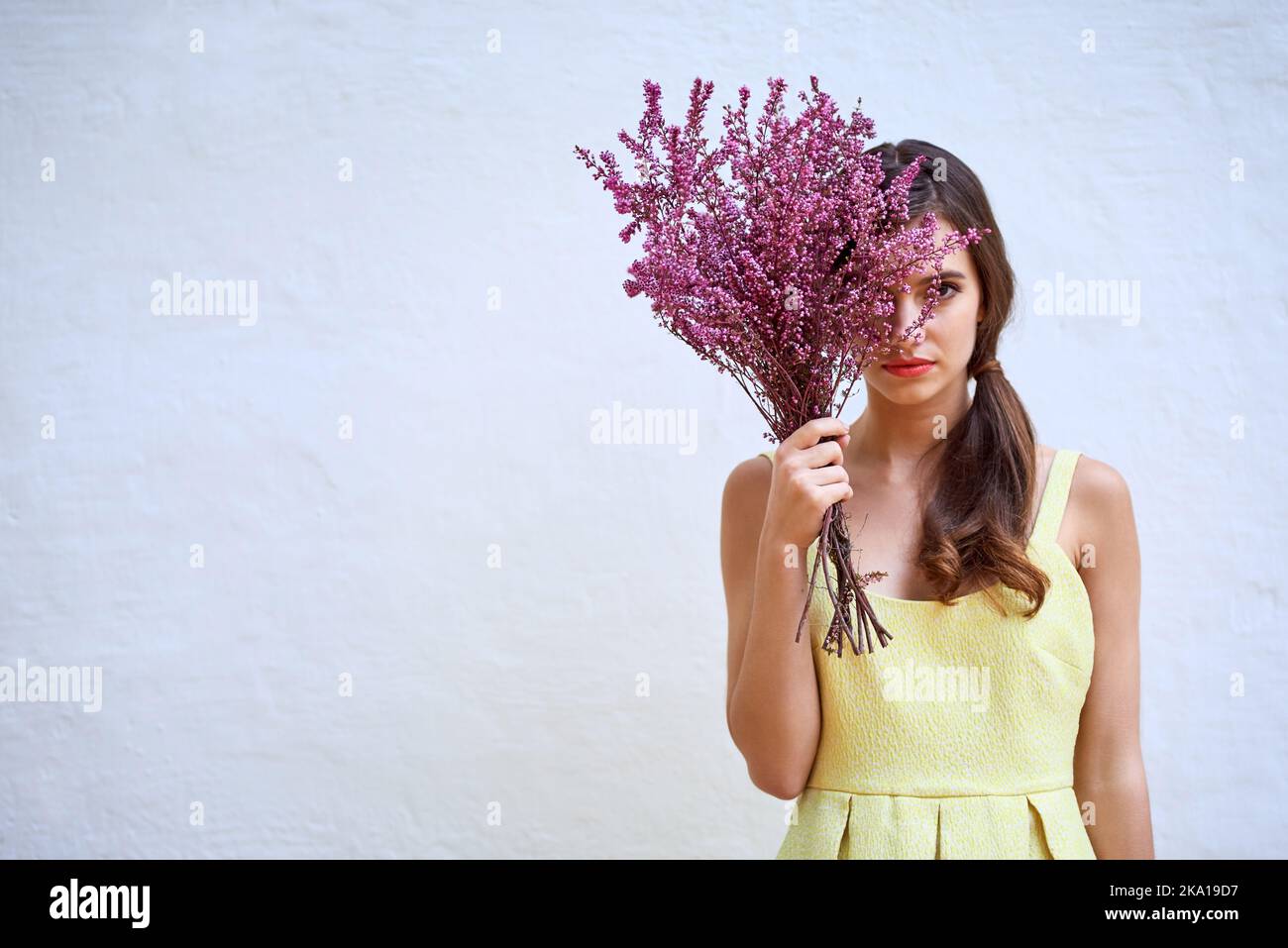 La bellezza la trova sempre. Studio ritratto di una giovane donna sicura che si nasconde dietro un bouquet di fiori in piedi su uno sfondo grigio. Foto Stock