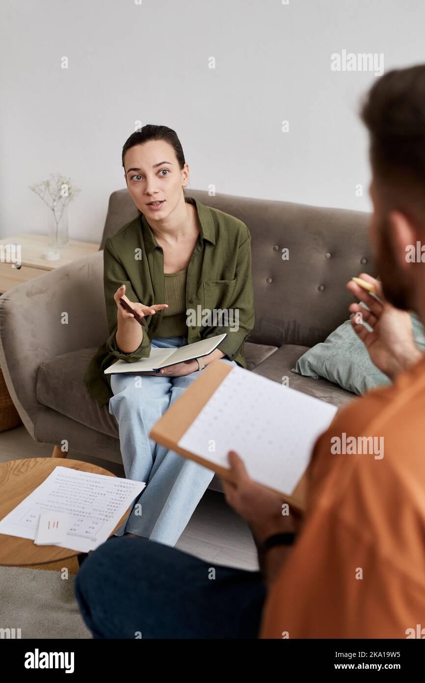 Tutor sicuro con copybook discutere nuovi argomenti con lo studente mentre si siede sul divano di fronte a lui a casa lezione Foto Stock