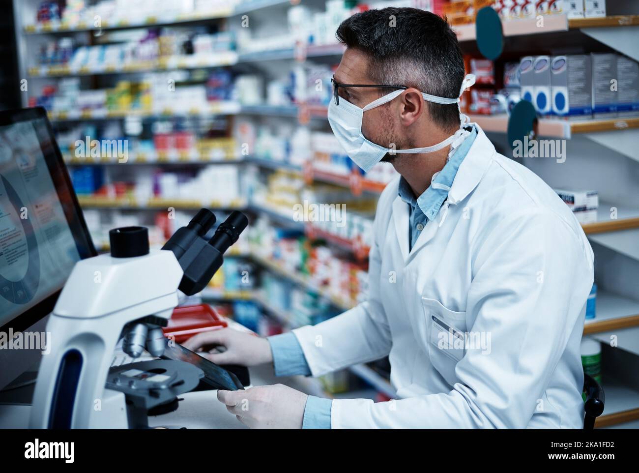 Compilare i dati per supportare la sua ricerca. Un uomo maturo che utilizza un tablet digitale e un computer mentre conduce ricerche farmaceutiche. Foto Stock
