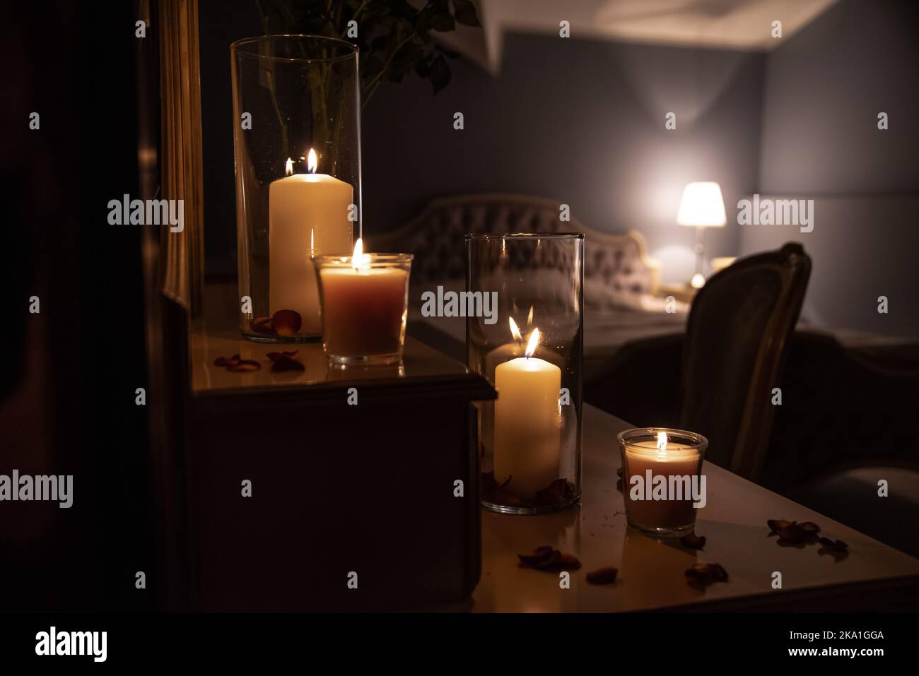 Vasetti di vetro con candele accese illuminano la camera, creando un'atmosfera romantica e calda nella camera da letto retrò con un bel decor sullo sfondo. Foto Stock