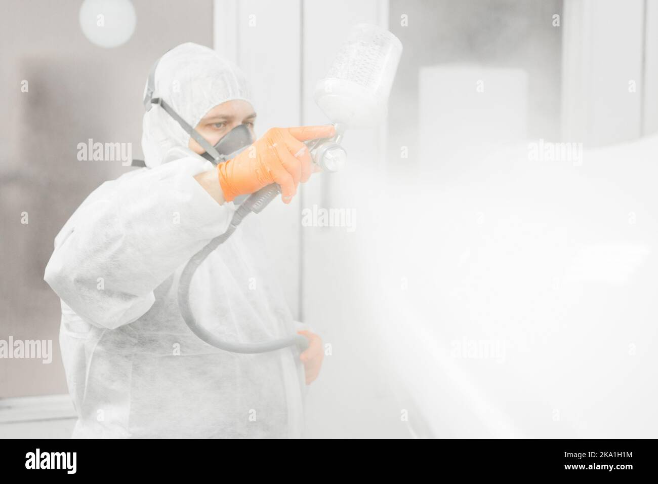 Il pittore professionista di automobile maschio sta dipingendo in garage dall'aerografo. L'uomo lavora con la pistola a spruzzo. Foto Stock