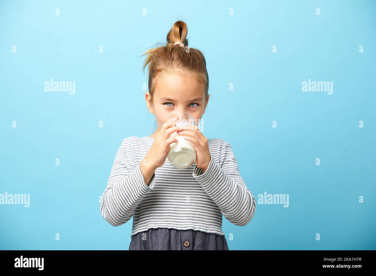 Ragazza carina di cinque anni beve latte su blu isolato. Foto Stock