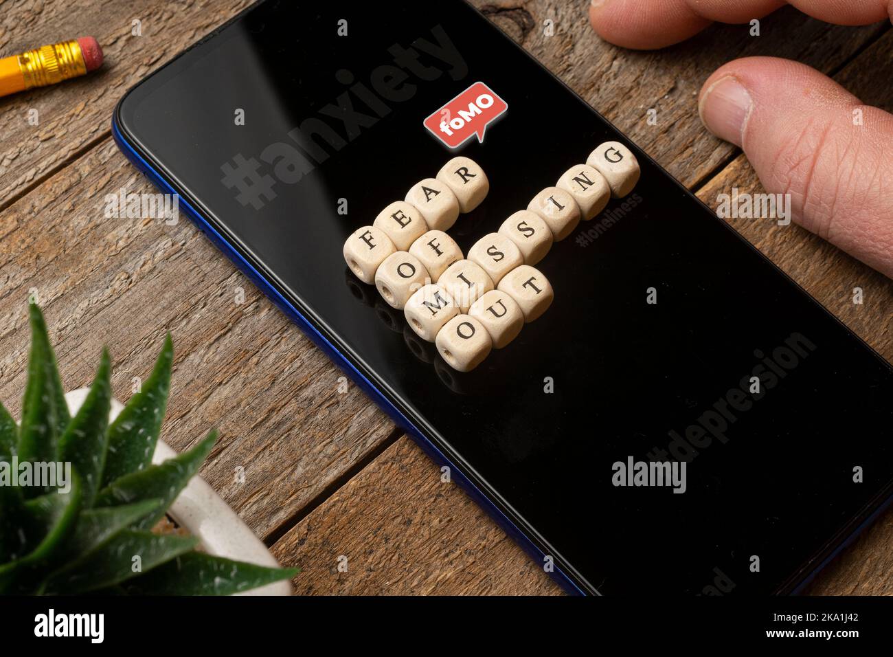 Concetto fomo (Fear of Missing out): Smartphone su un tavolo di legno con qualche dado che compone una frase. Foto Stock