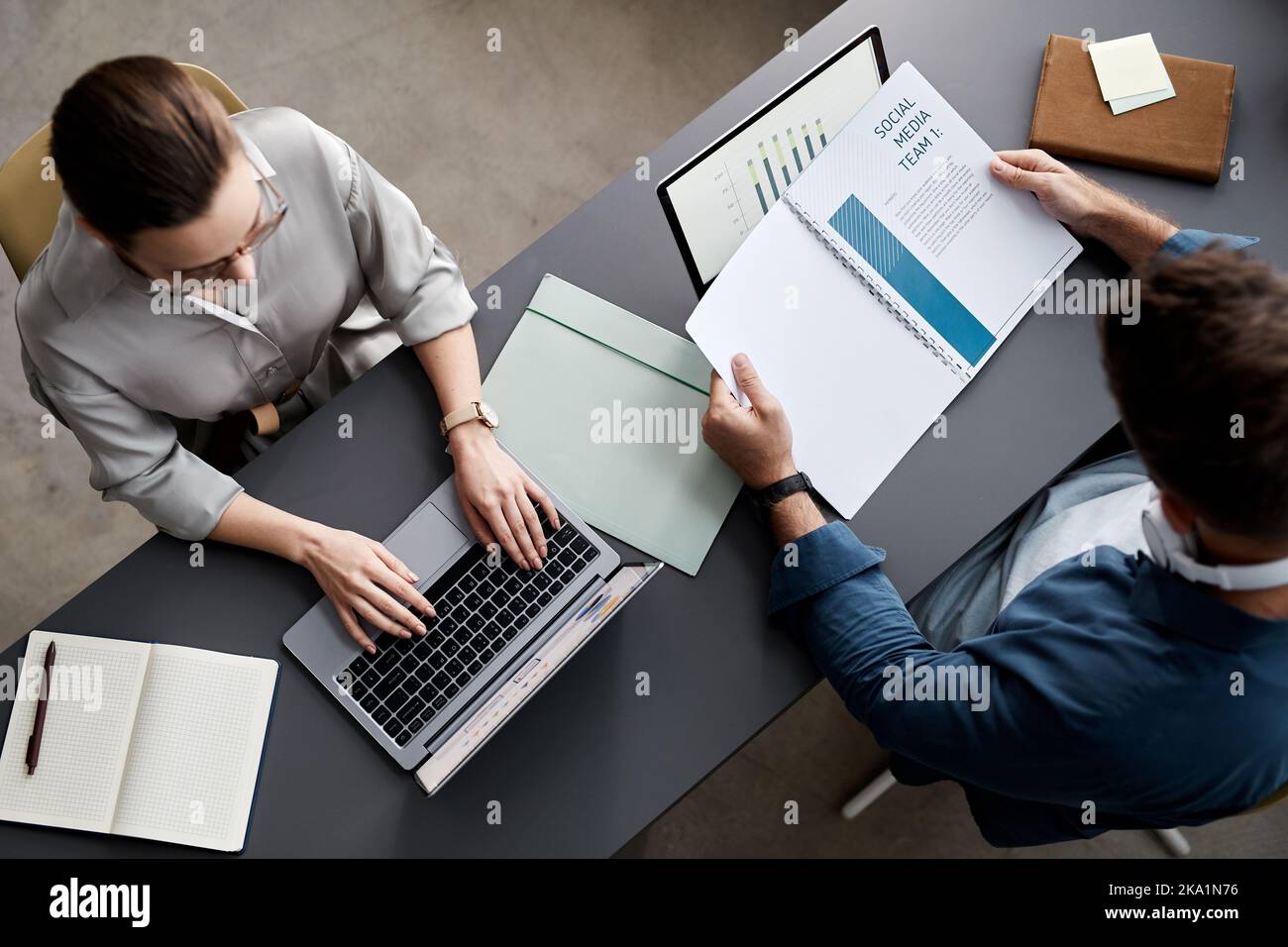 Immagine sopra di due giovani economisti seduti sul posto di lavoro davanti ai computer portatili e che lavorano con informazioni e documenti finanziari Foto Stock