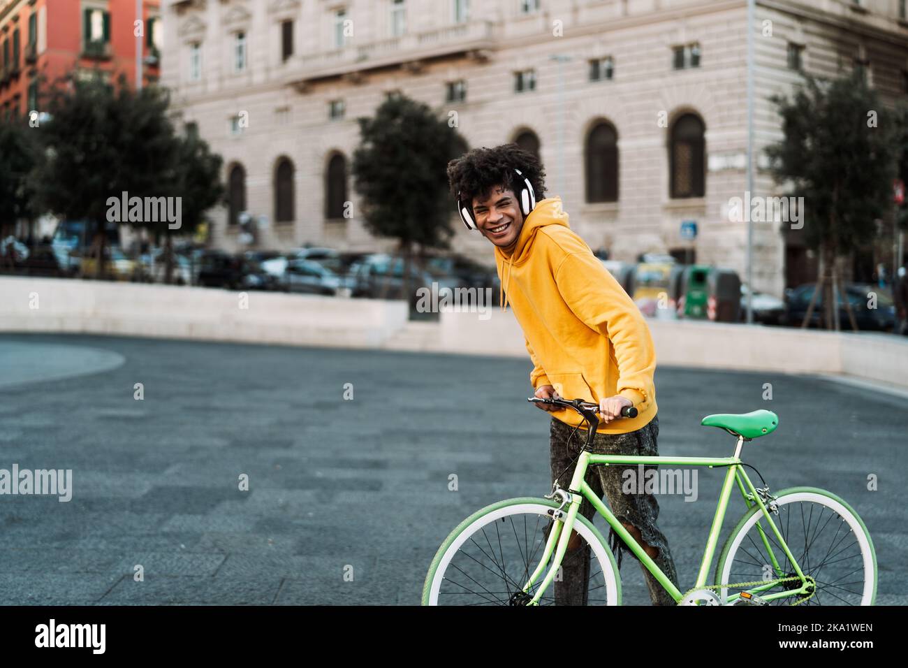 Buon giovane africano che si diverte con la bicicletta in città mentre ascolti musica con le cuffie Foto Stock