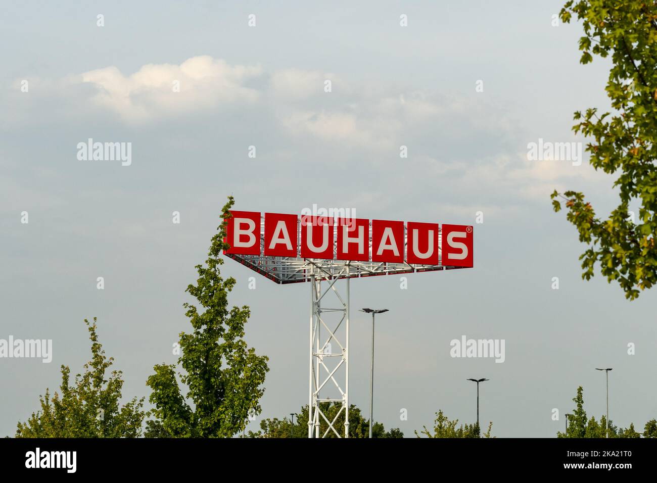 Le lettere Bauhaus del negozio di ferramenta tedesco in alto nel cielo. Pubblicità su un parcheggio. Gli alberi verdi sono davanti al cielo nuvoloso. Foto Stock