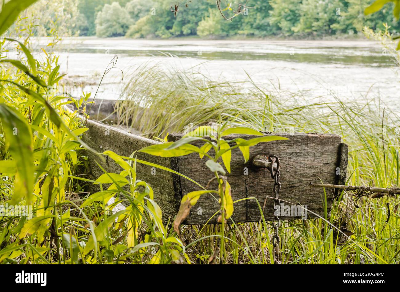 Barche da pesca in legno legate alla riva. Una vista di una piccola barca da pesca in legno derelict, coltivata di erbacce, ormeggiata sulla riva del lago in autum Foto Stock