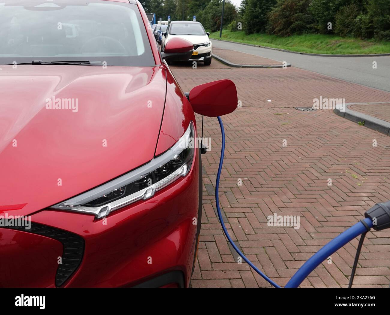 Faro di una Ford Mach-e rossa completamente elettrica primo piano. L'auto viene addebitata in un ampio parcheggio nei Paesi Bassi Foto Stock
